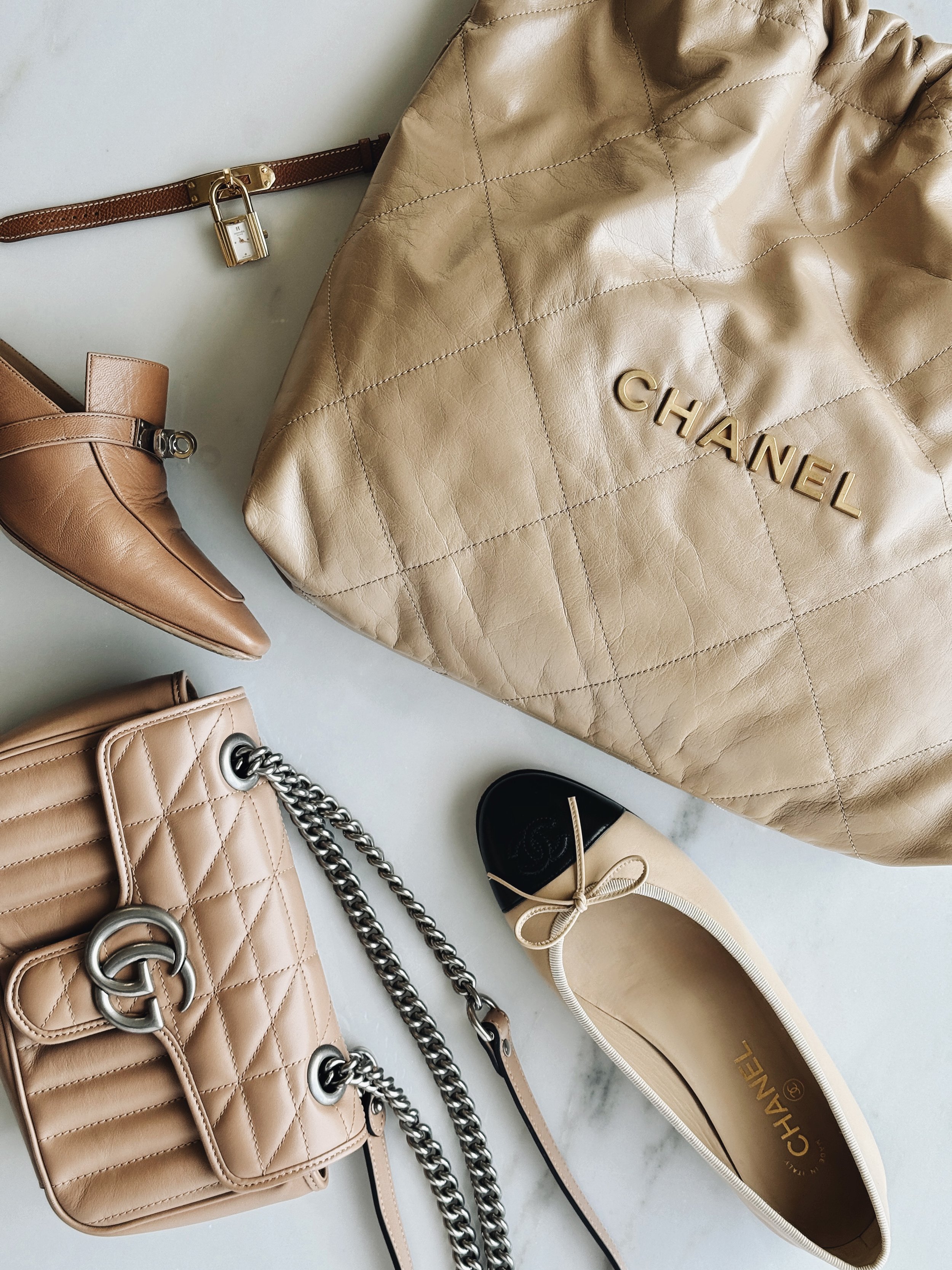 chanel, gucci, and hermes products displayed in a flat lay on a white marble table