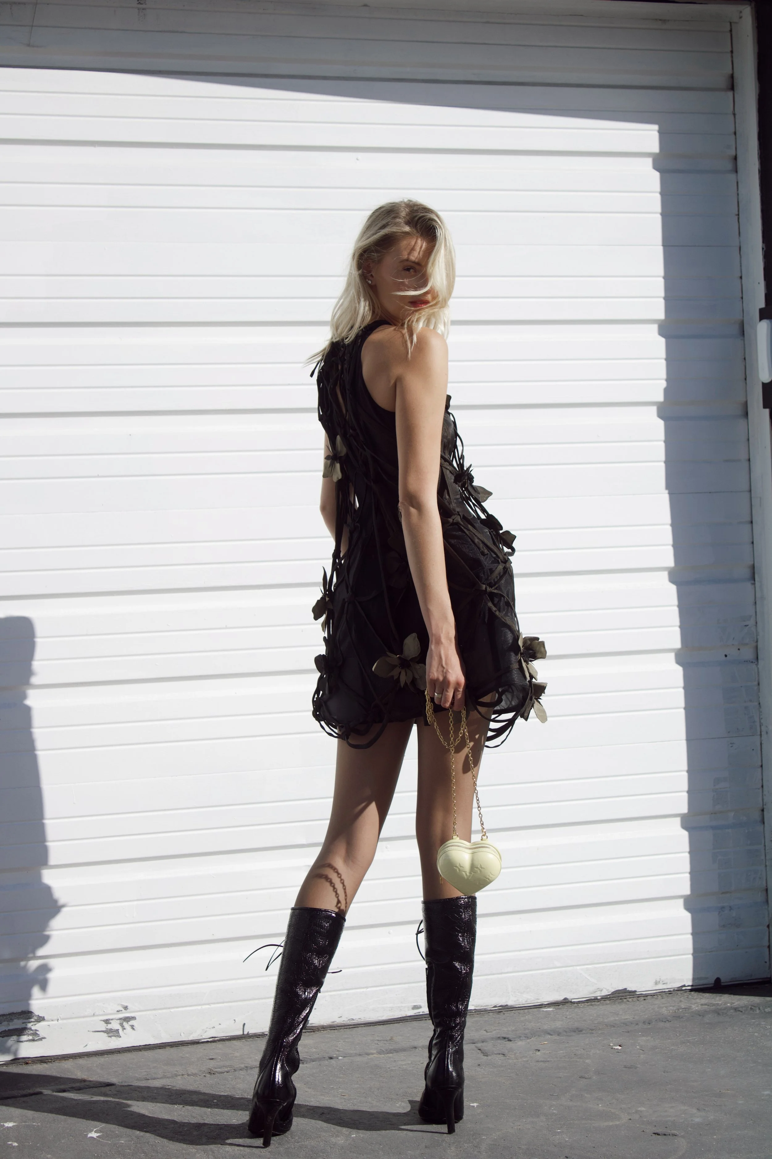 a model stands in an industrial area while wearing a brown floral mini dress, lace up boots, and a louis vuitton vernis heart bag