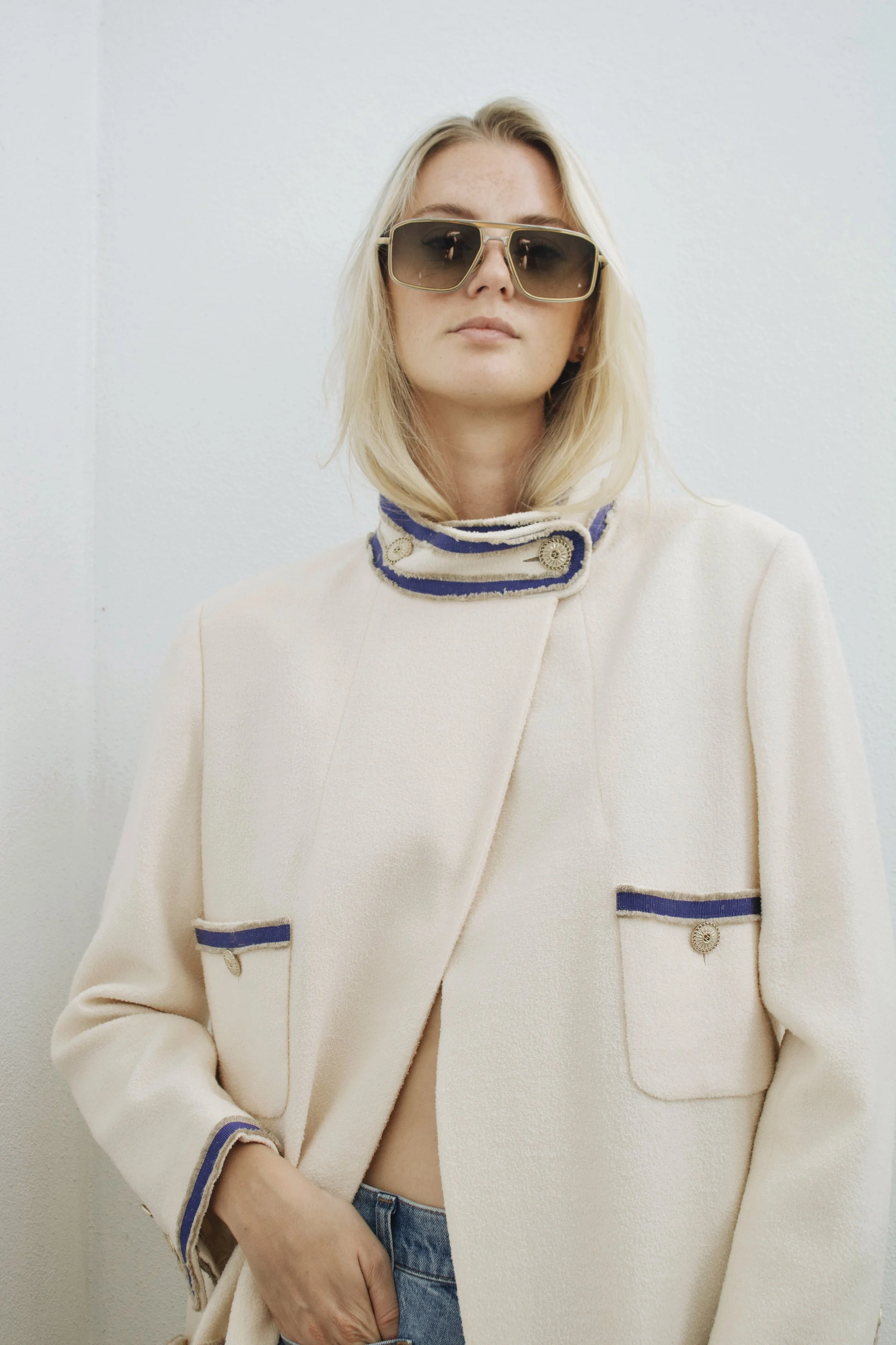 a model wears sunglasses and a long chanel coat with her hand tucked in her jeans pocket