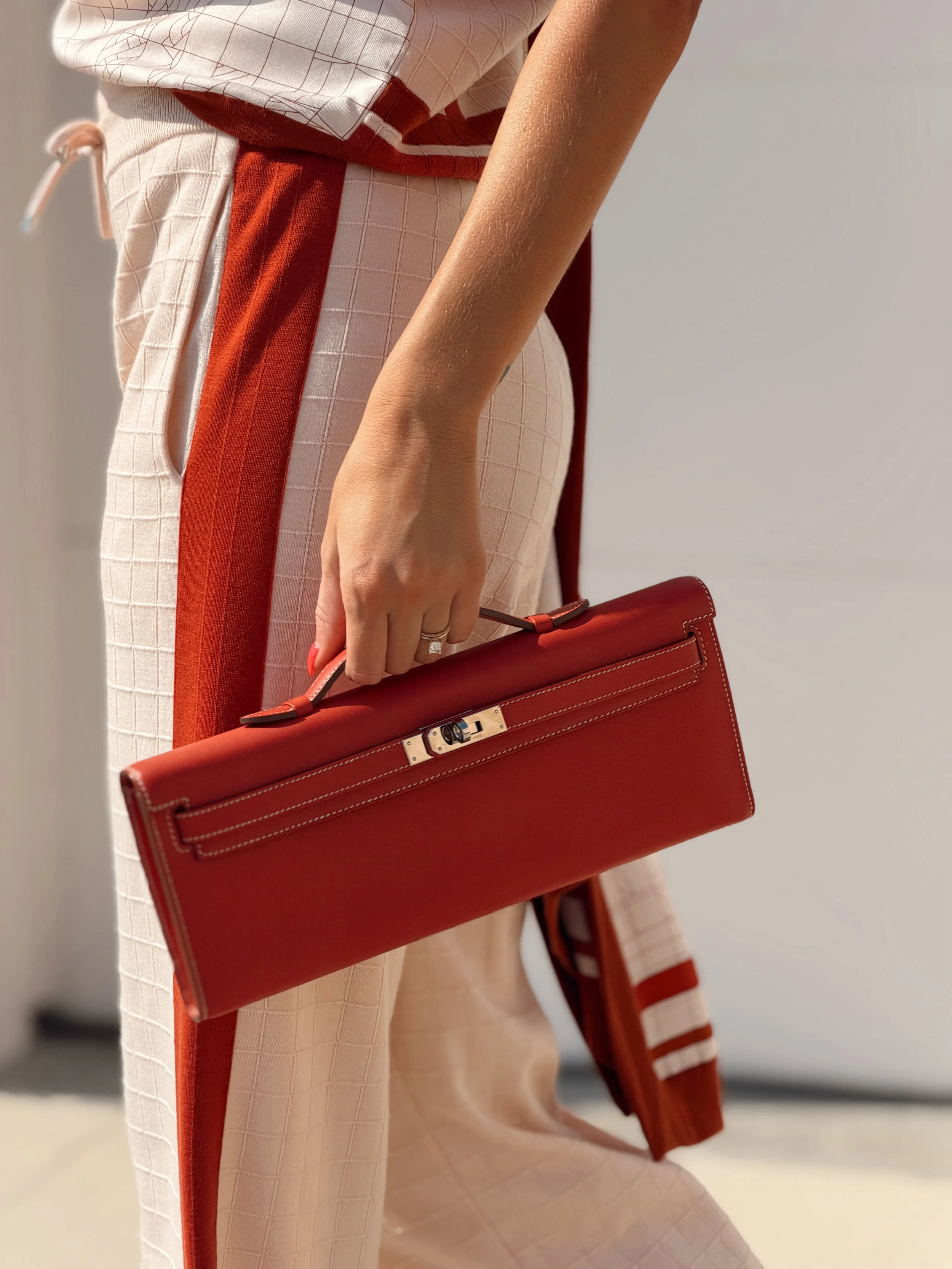 a close up photo of a model walking by with an hermes kelly cut bag in red while wearing an hermes top and pants set