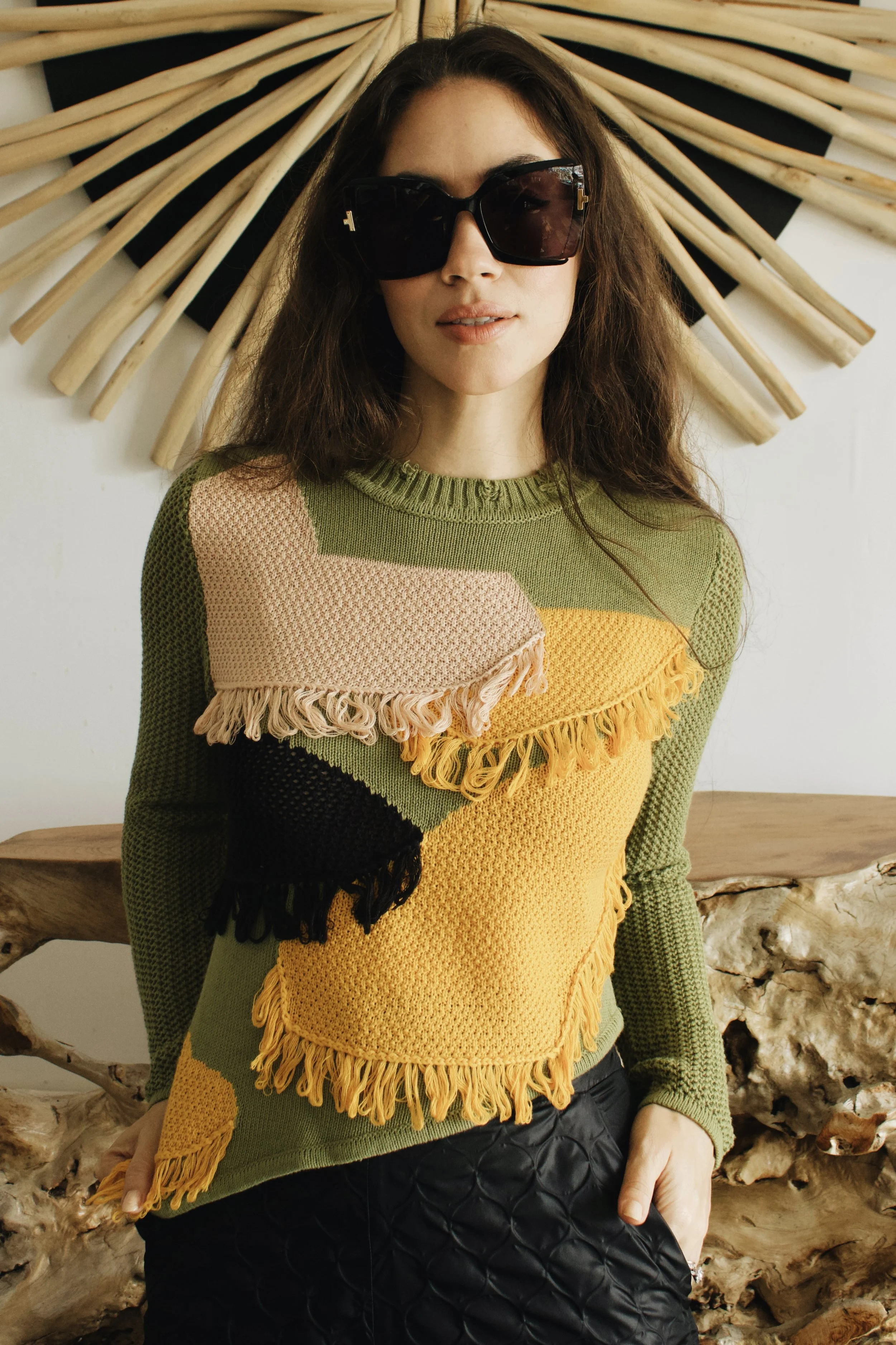 a model wears a designer sweater and sunglasses while posing in front of a beautiful wooden table