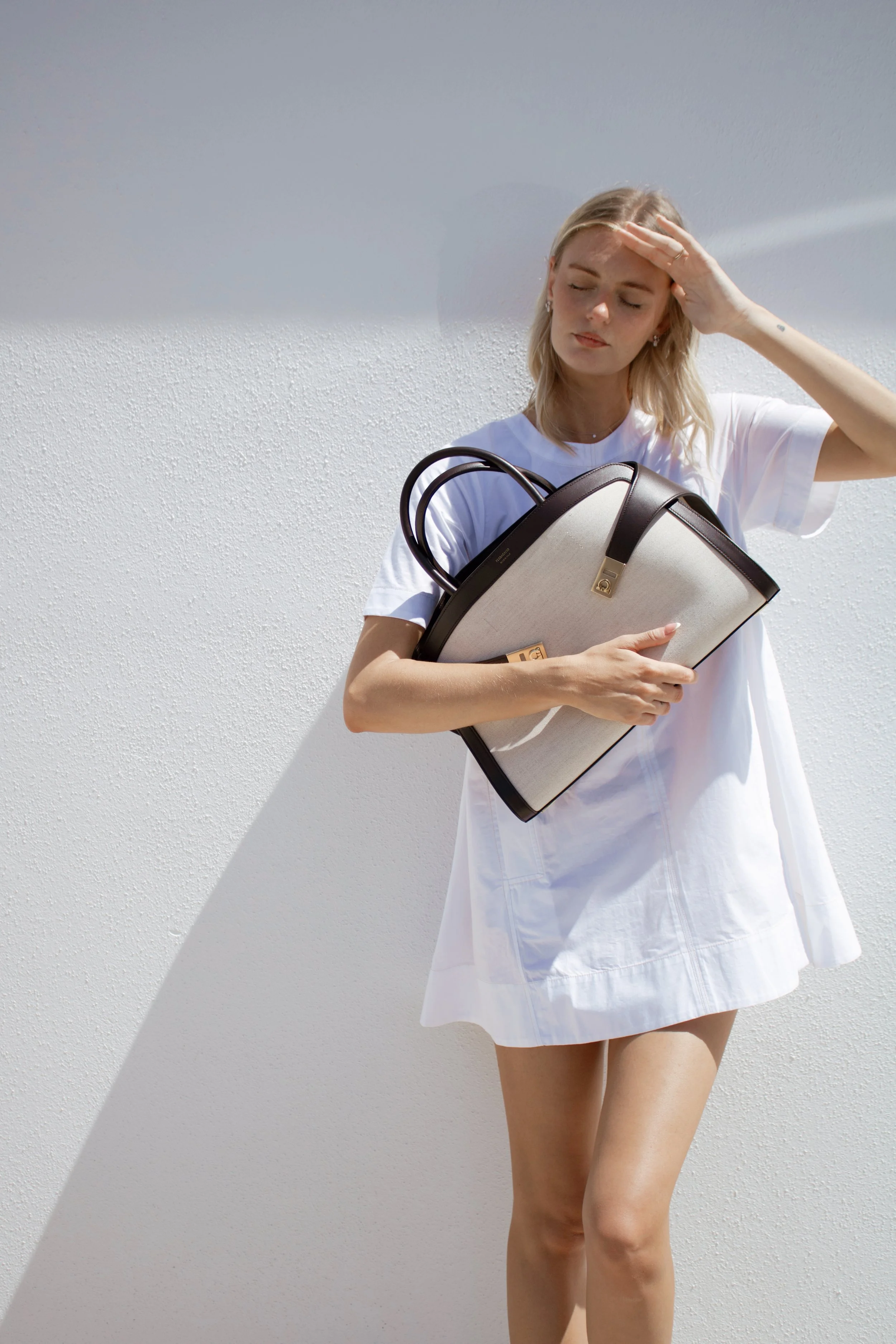 editorial fashion photoshoot featuring a model in a white dress holding the salvatore ferragamo large hug bag