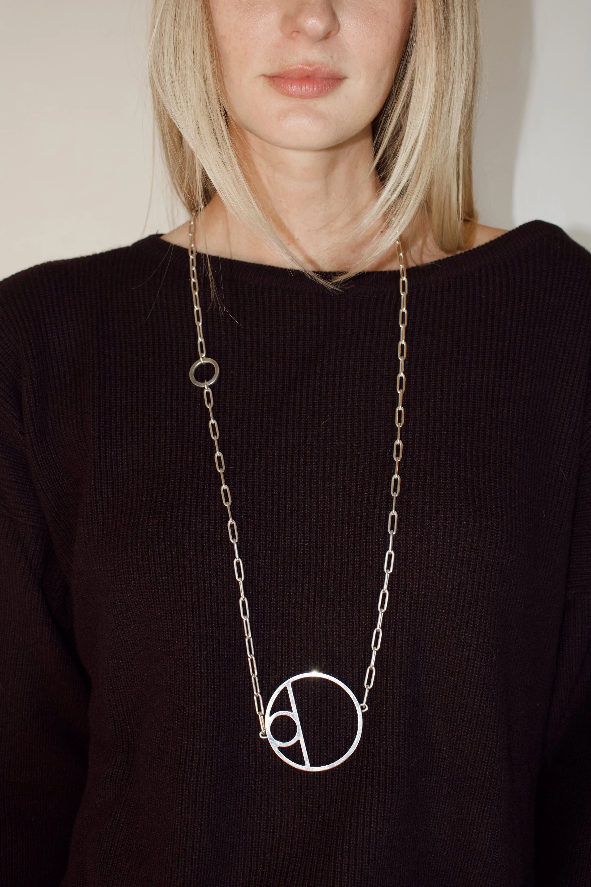 a model stands in the studio wearing a brown sweater and a silver hermes necklace