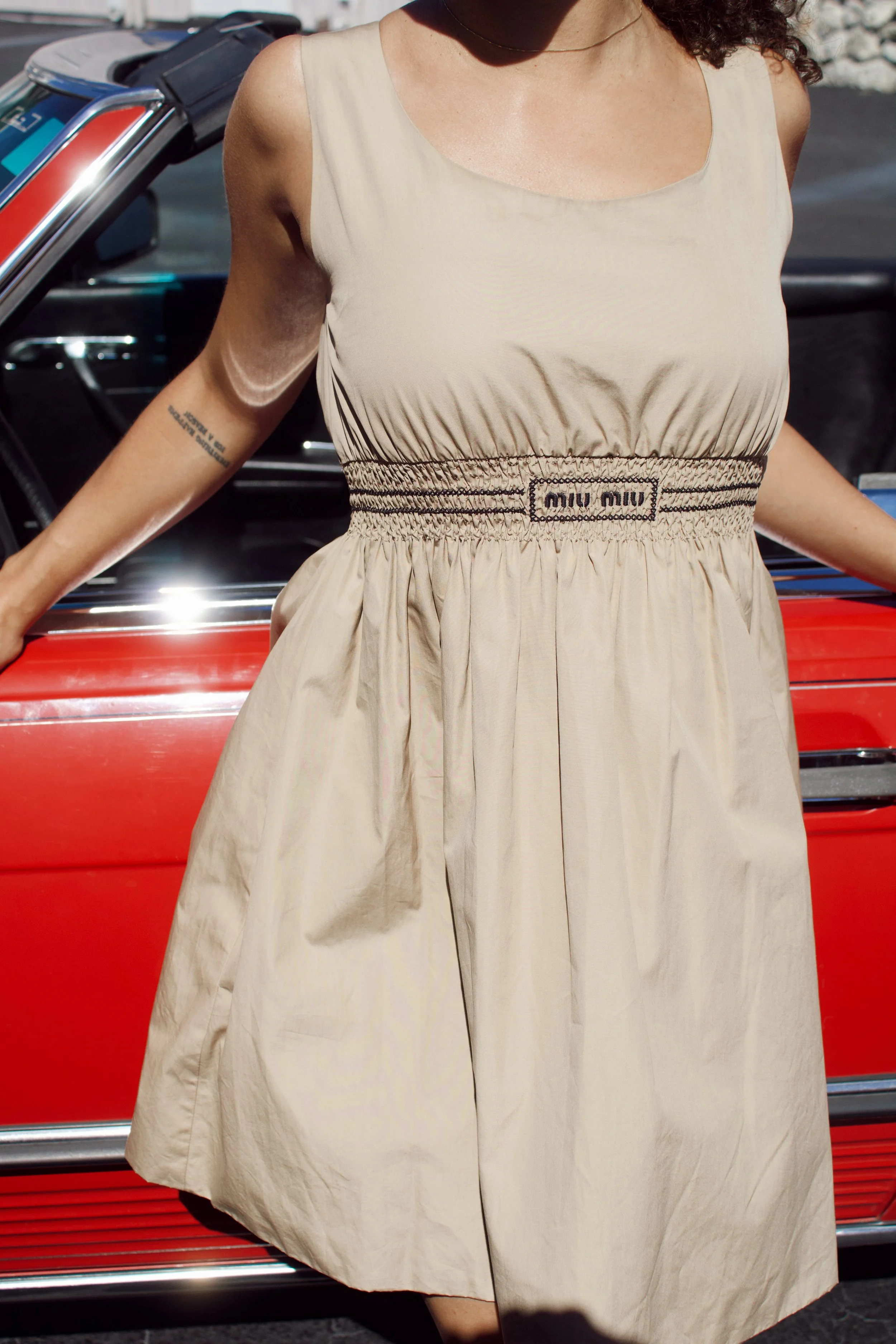 model stands in front of a red vintage mercedes wearing a tan miu miu dress
