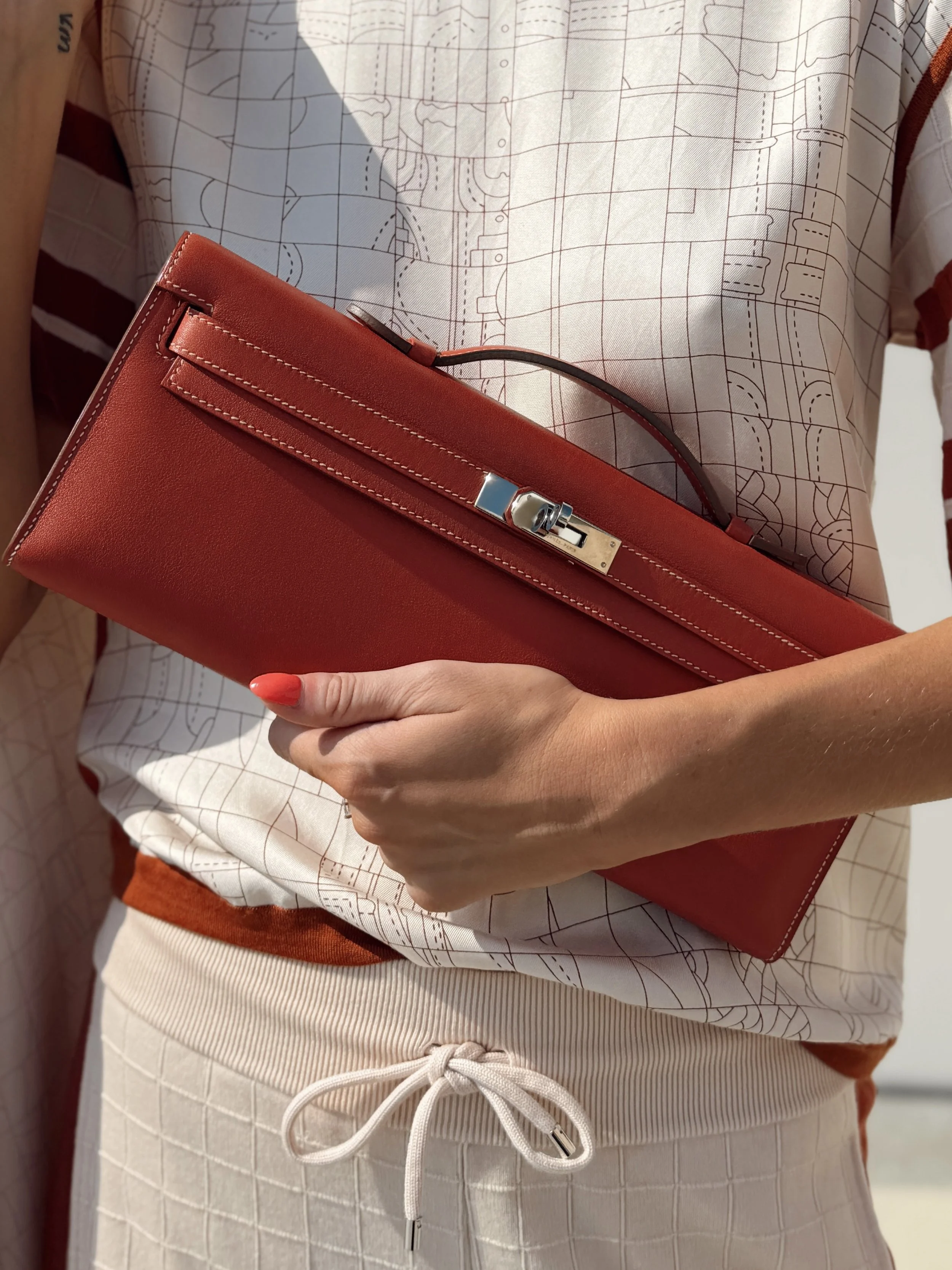 a close up photo of an hermes kelly cut bag in red held by a model wearing an hermes top and pants set