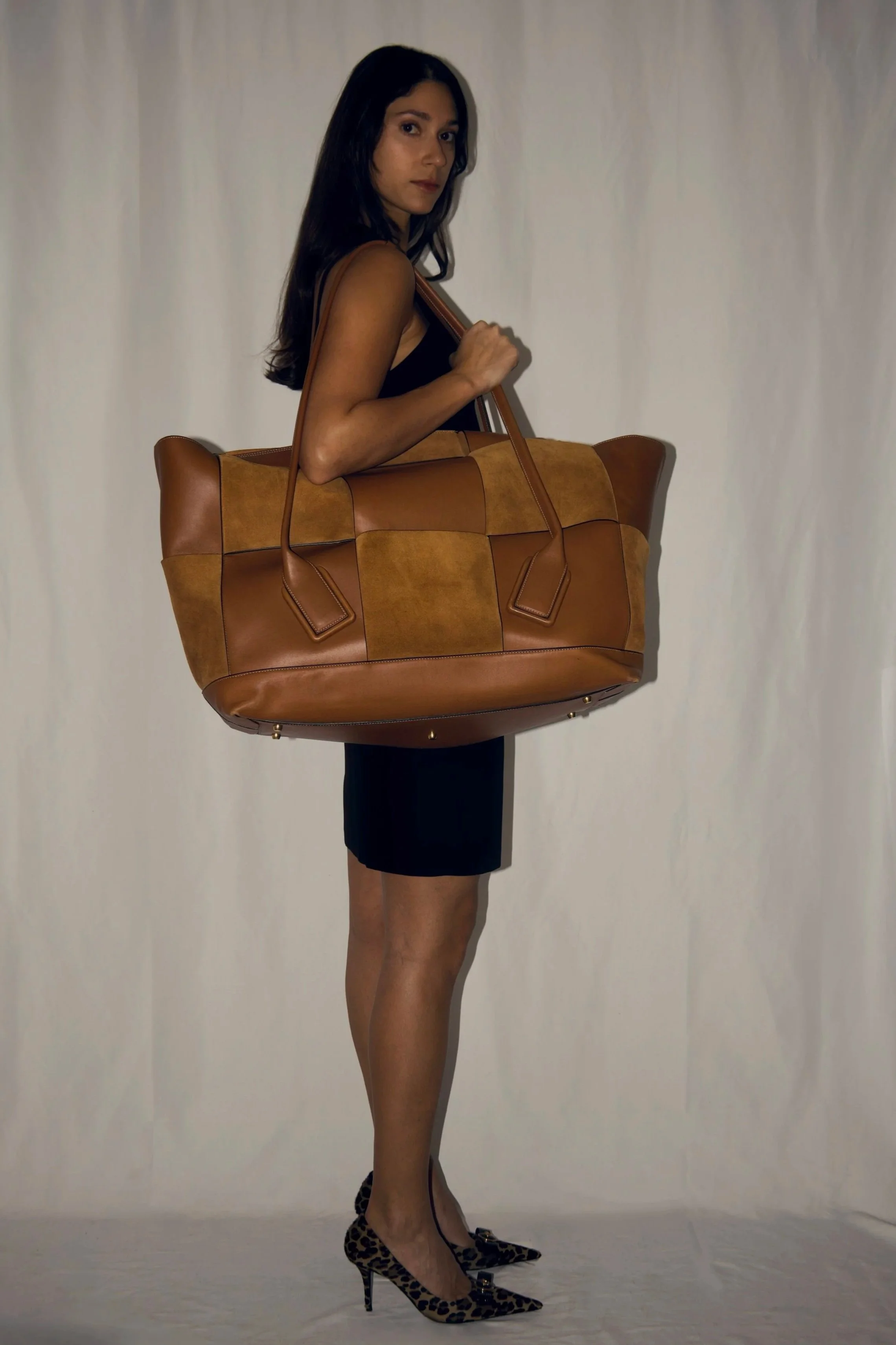 a studio photoshoot of a model wearing the bottega veneta maxi arco bag and versace animal print heels