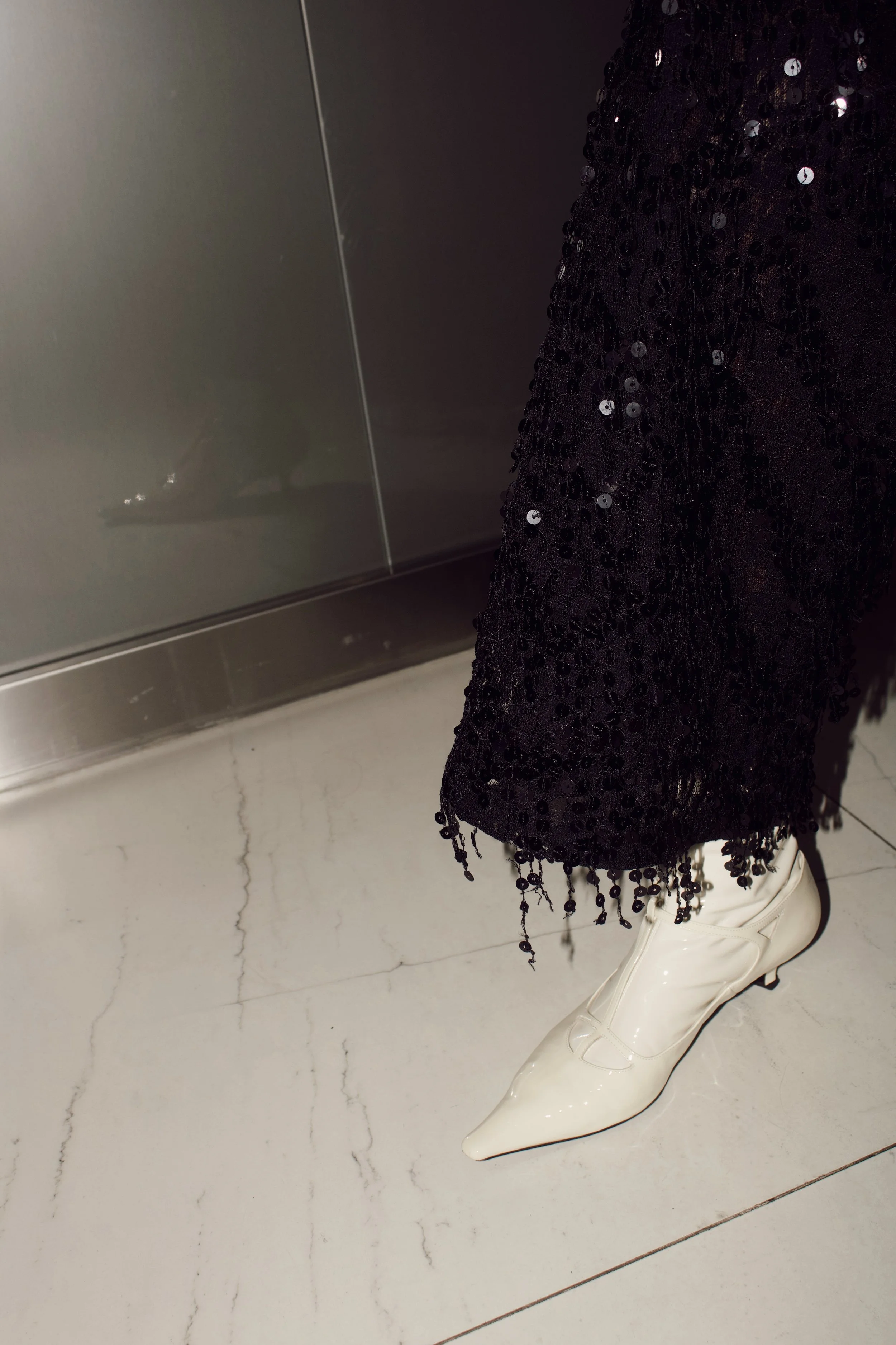 a close up flash photograph of a model wearing The Row cream patent leather boots while standing in an elevator