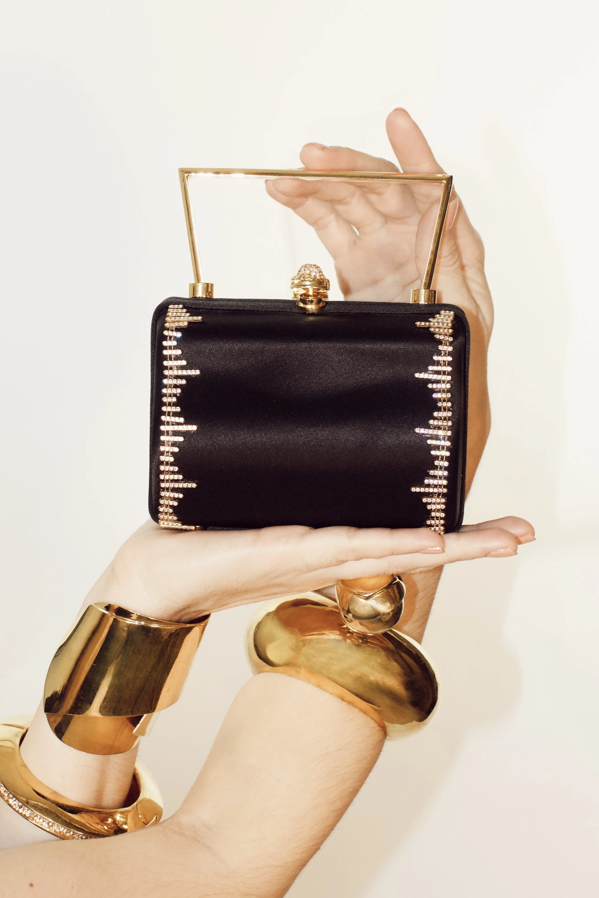 two arms hold up a judith leiber bag while wearing gold alexis bittar jewelry