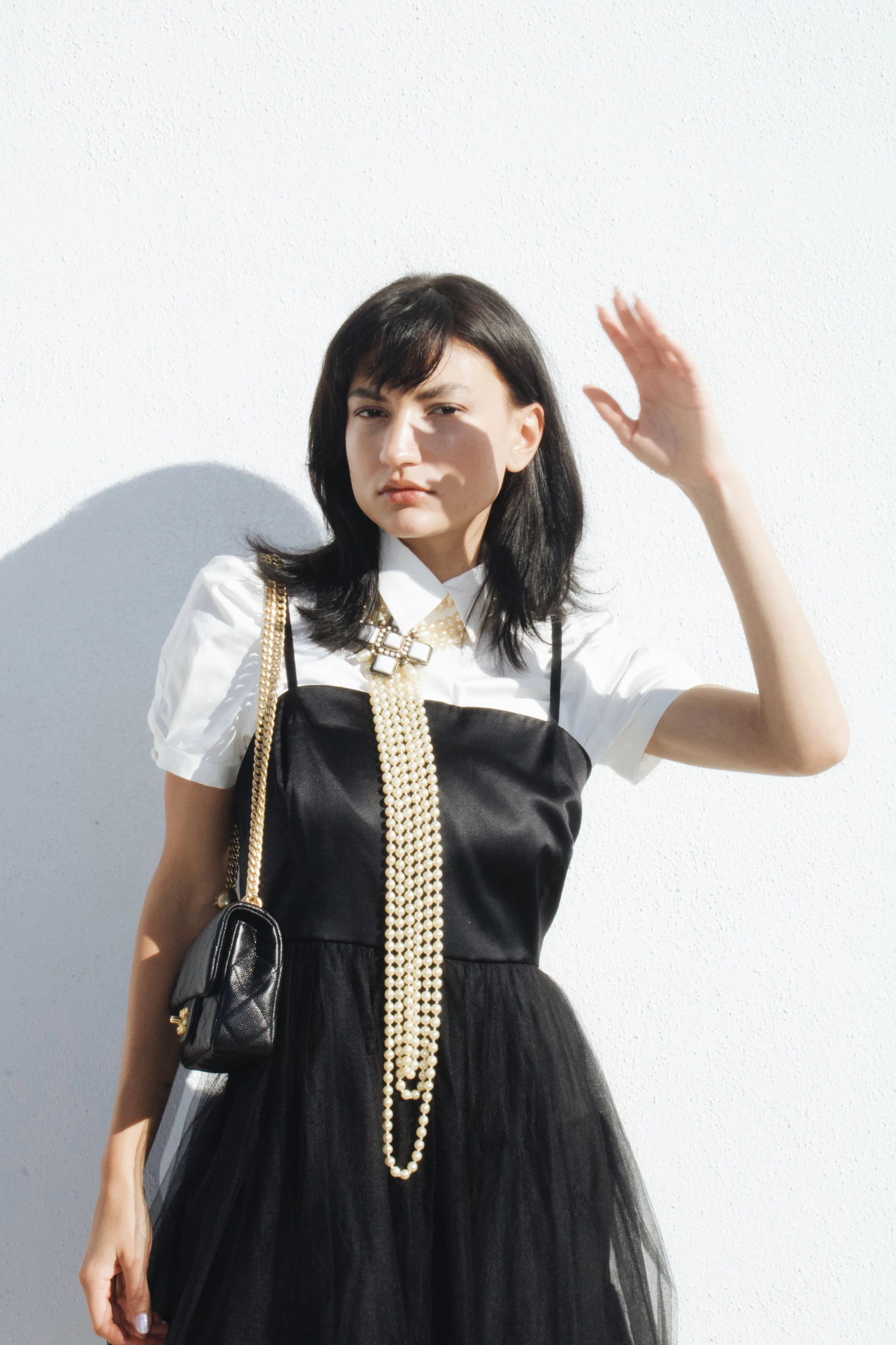 model wears a black dress with a white shirt and a vintage long pearl chanel necklace