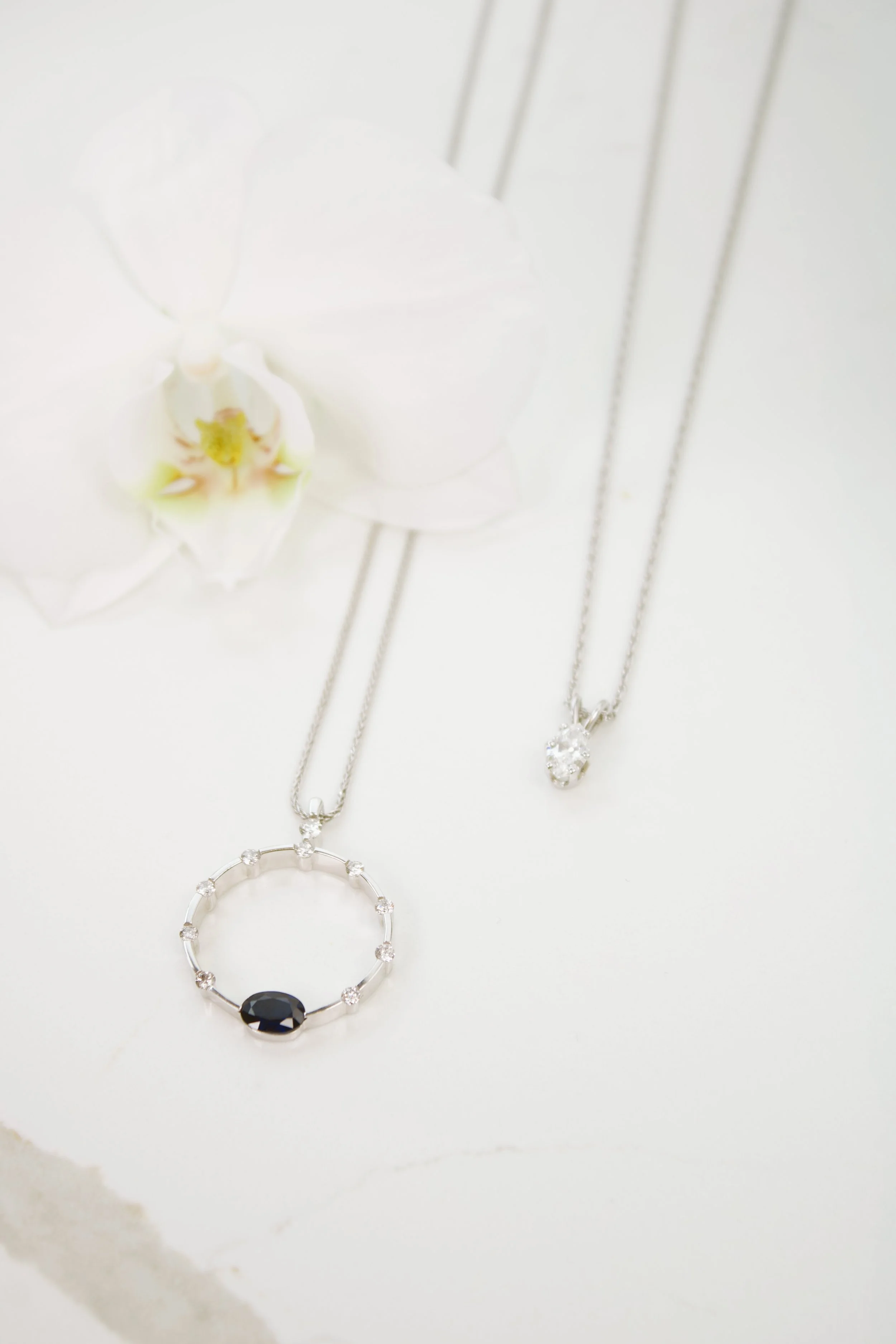 product shoot with two white gold necklaces on a marble table with orchid