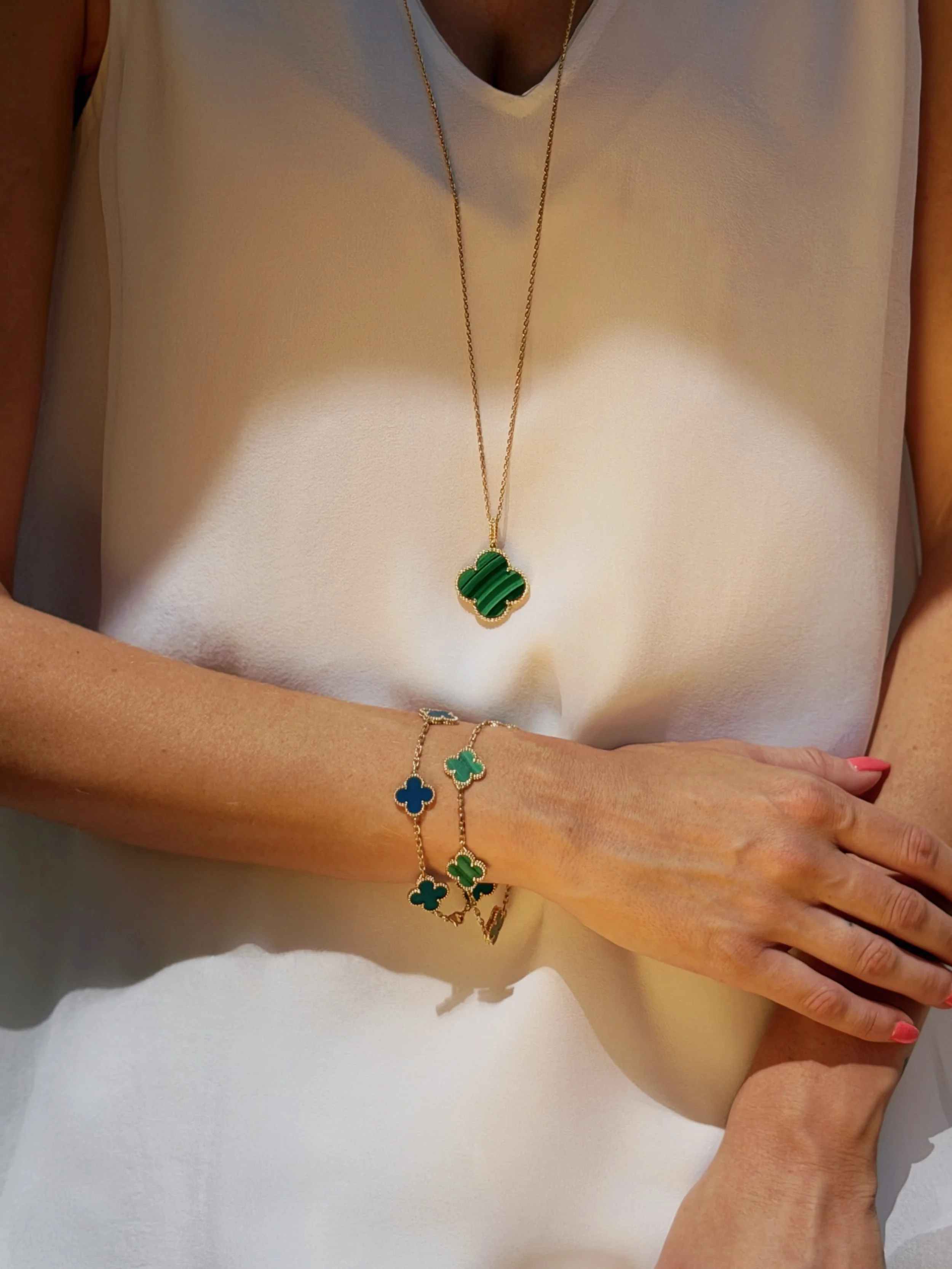 a close up photo of a model wearing a Van Cleef and Arpels Alhambra necklace and two four motif bracelets