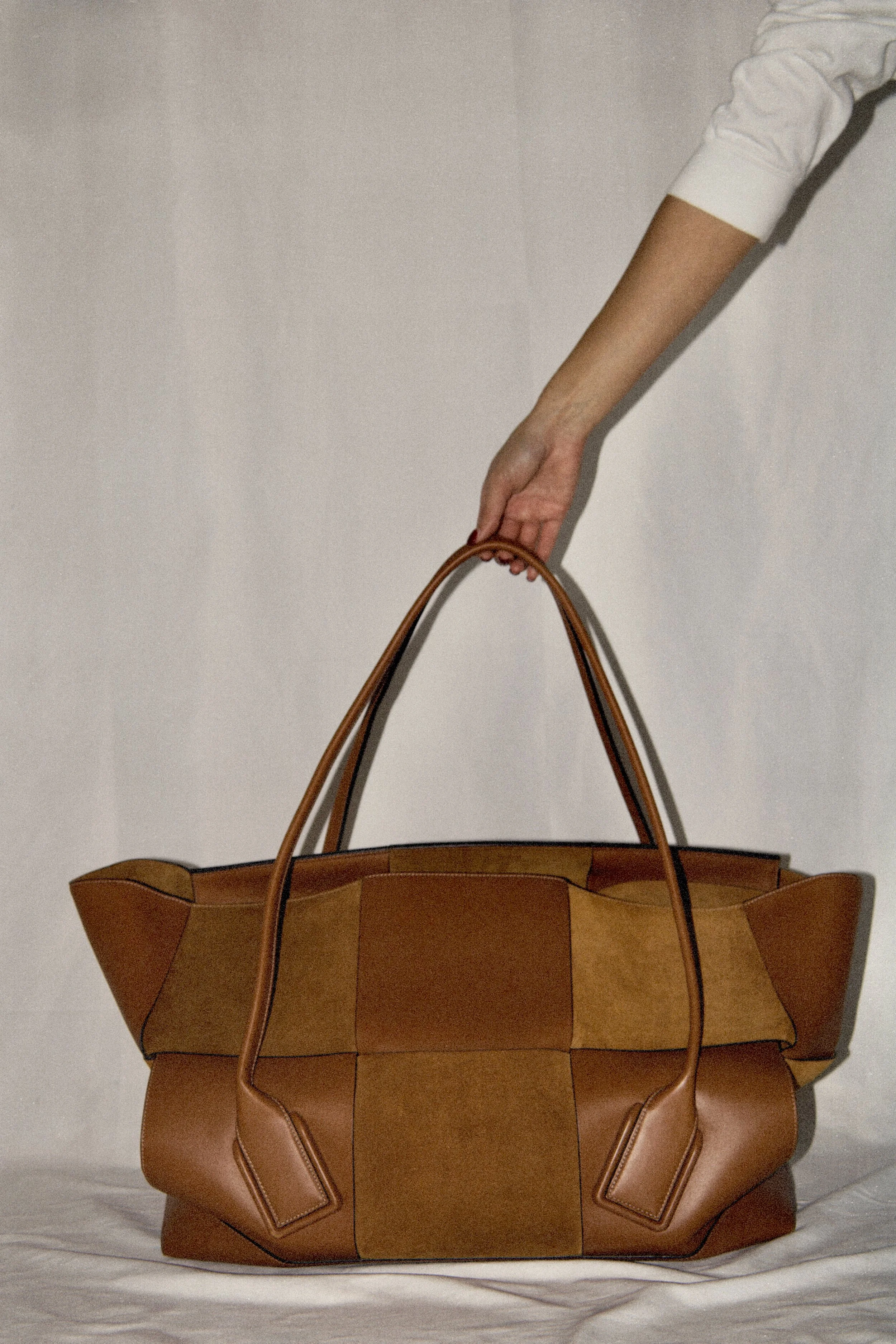 a studio image of a model reaching for a tan bottega veneta maxi arco bag