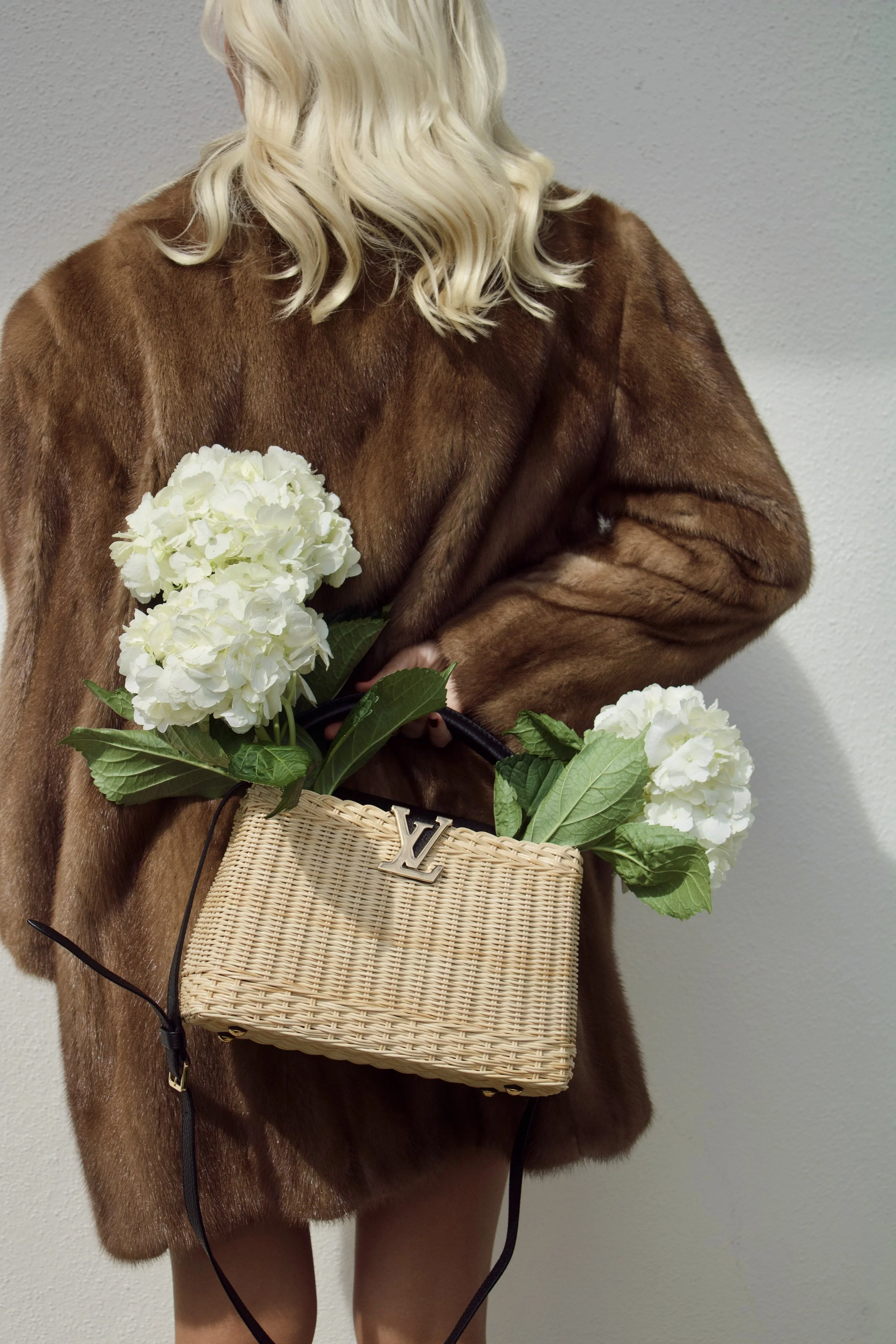 a model wears a vintage fur coat holding a louis vuitton wicker capucines bag