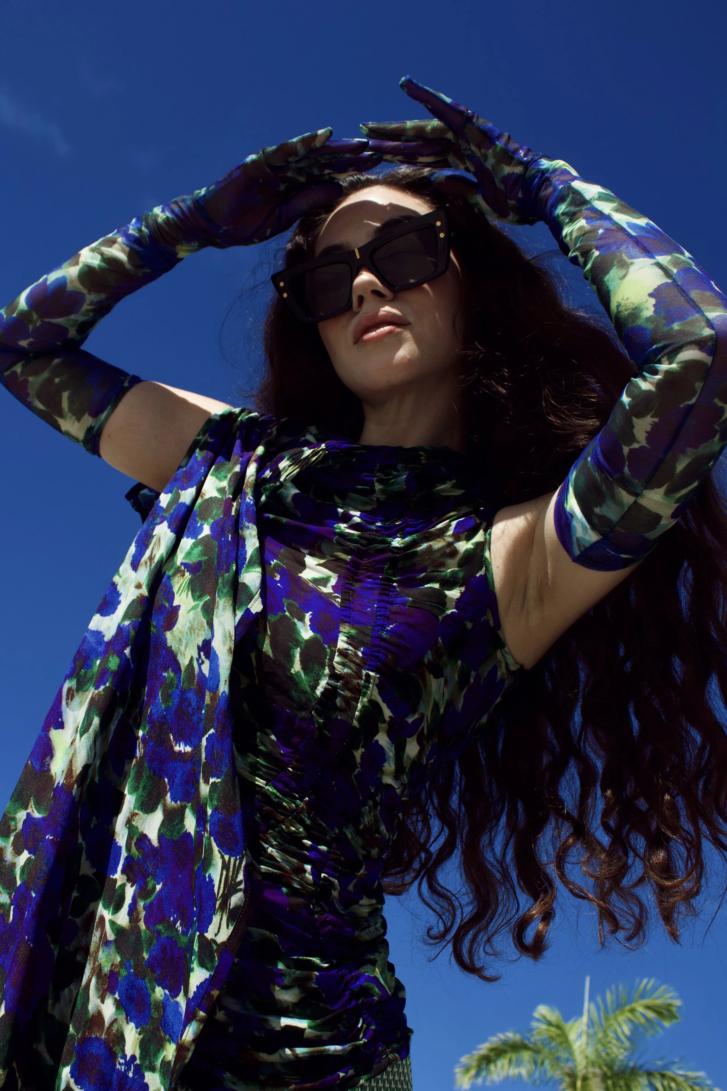 a close up photo of a model wearing dries van noten top and gloves with blue sky in the background