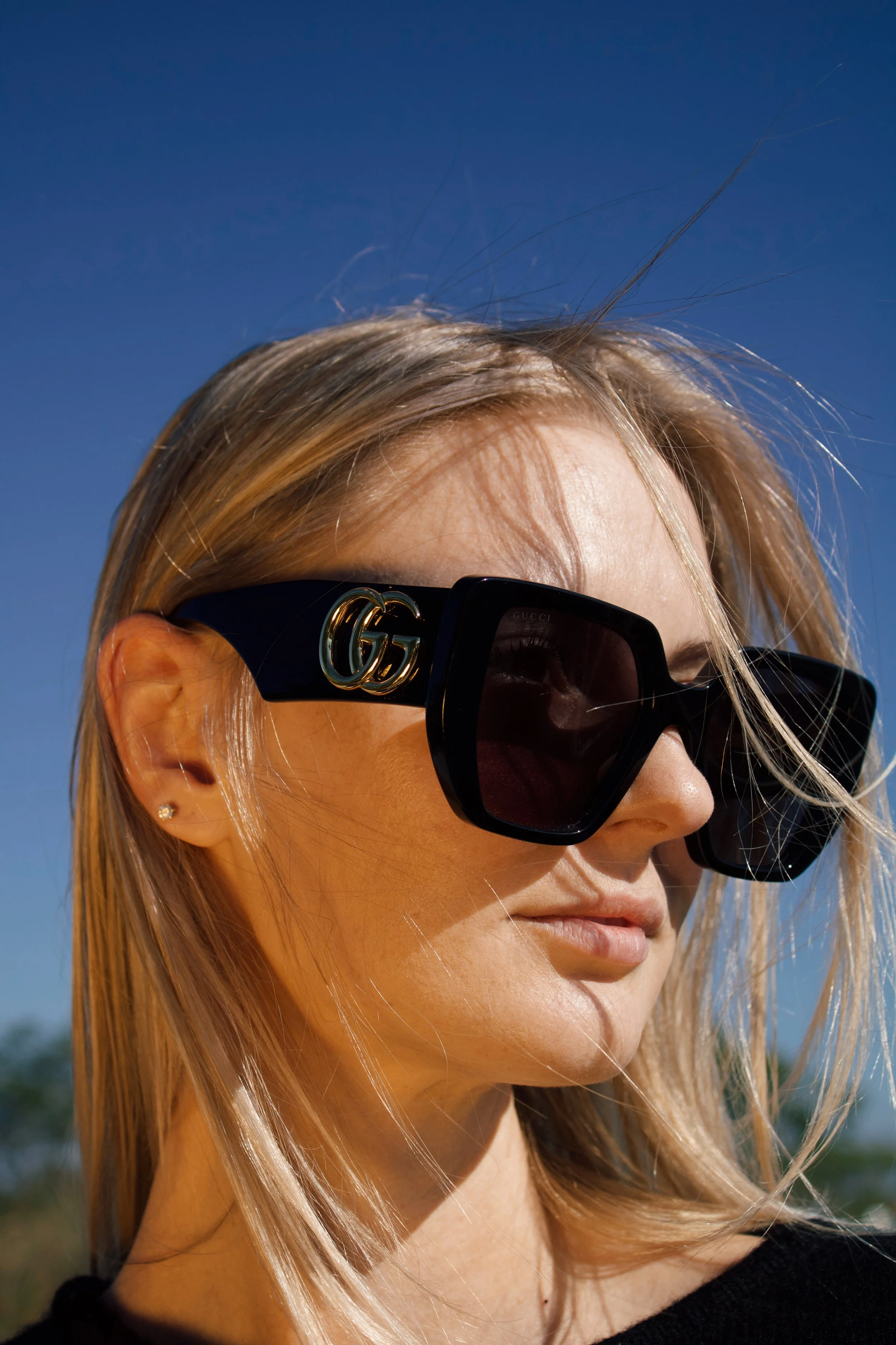 a close up photo of a model wearing black oversized gucci sunglasses with golden light shining on her face