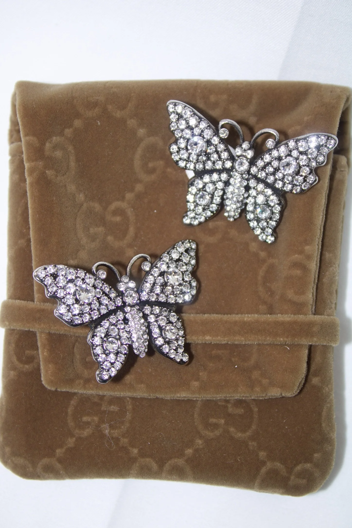 gucci butterfly rhinestone earrings on top of a gucci brown velvet jewelry pouch
