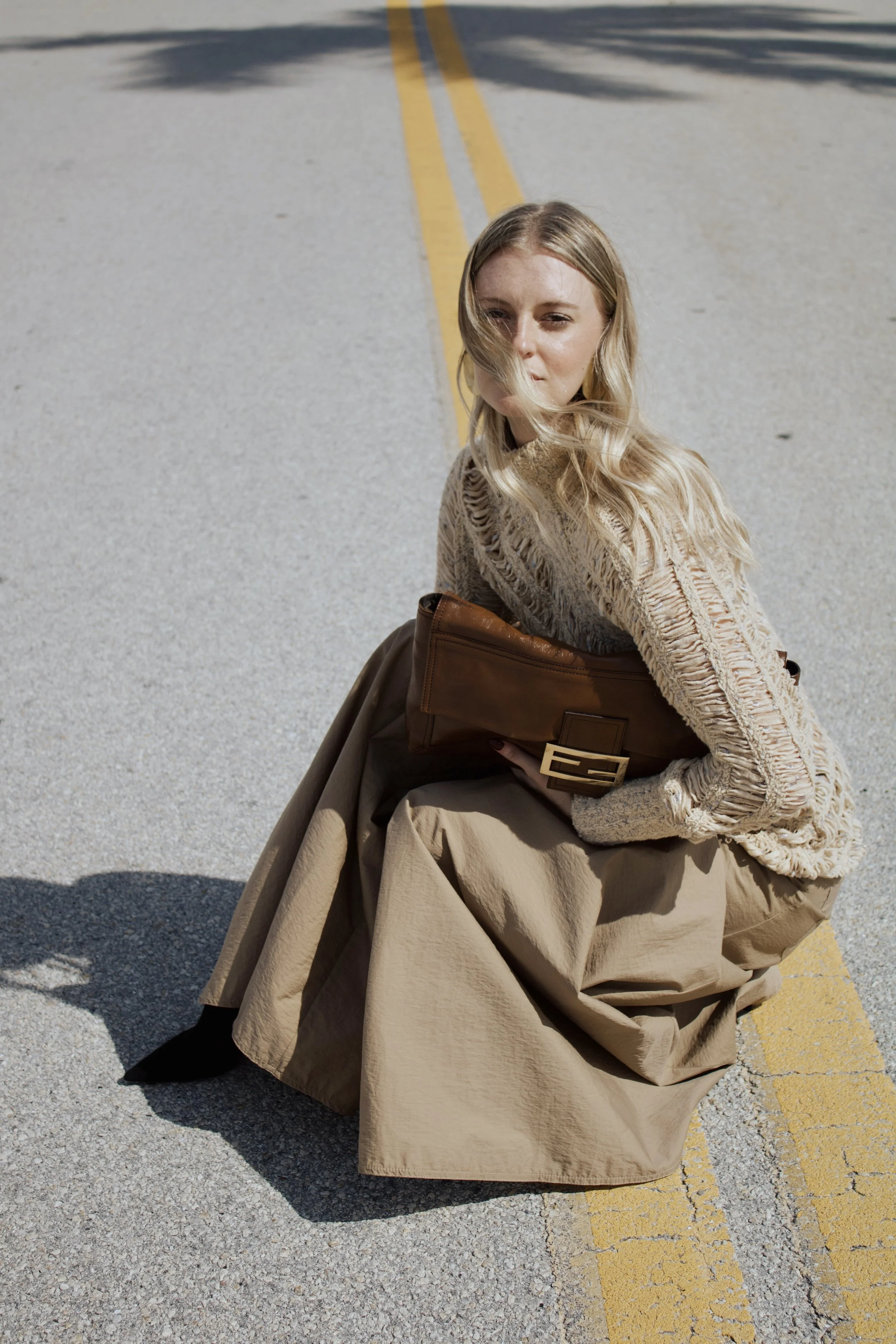 editorial fashion photoshoot featuring a model posing in the street holding an extra large fendi baguette bag