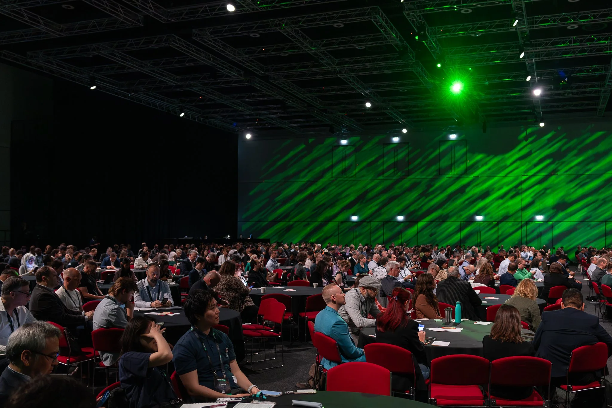 Quantum Australia Conference room filled with many attendees seated at tables, facing a stage with green lighting effects on the wall and ceiling.