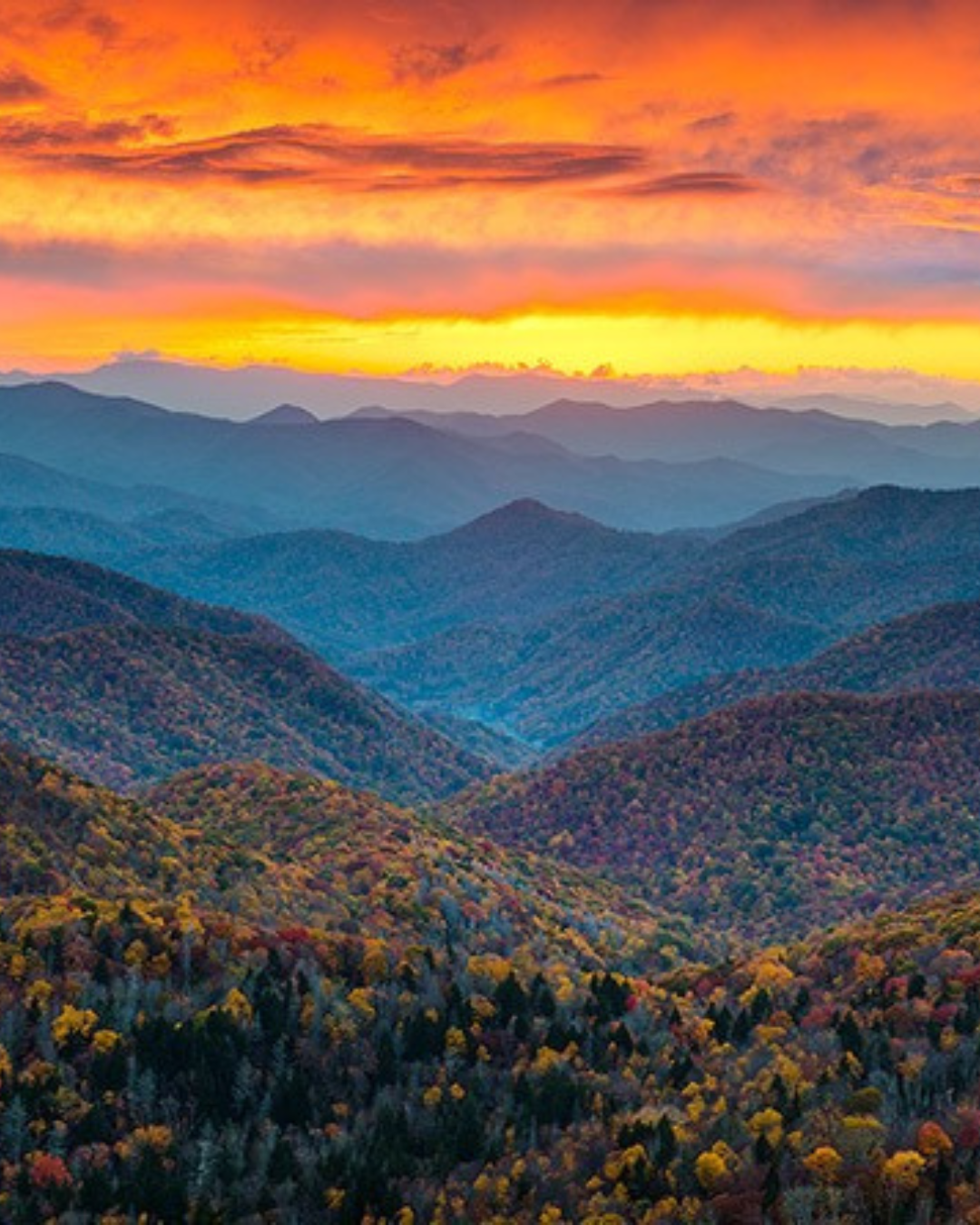 View from peak of mountain into the valleys of Blue Ridge Mountains with orange and yellow sunset above