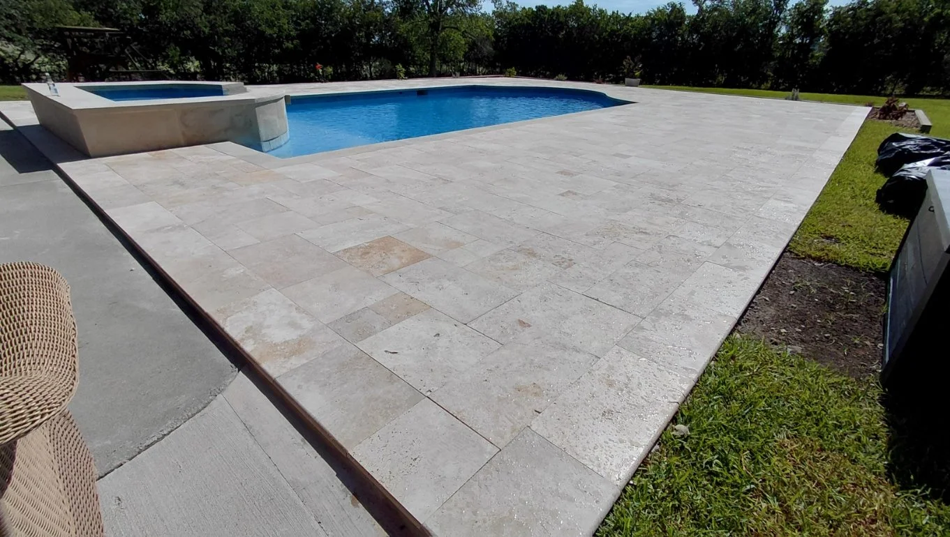 View of a large travertine pool deck wrapped around a pool and spa in Westlake Texas