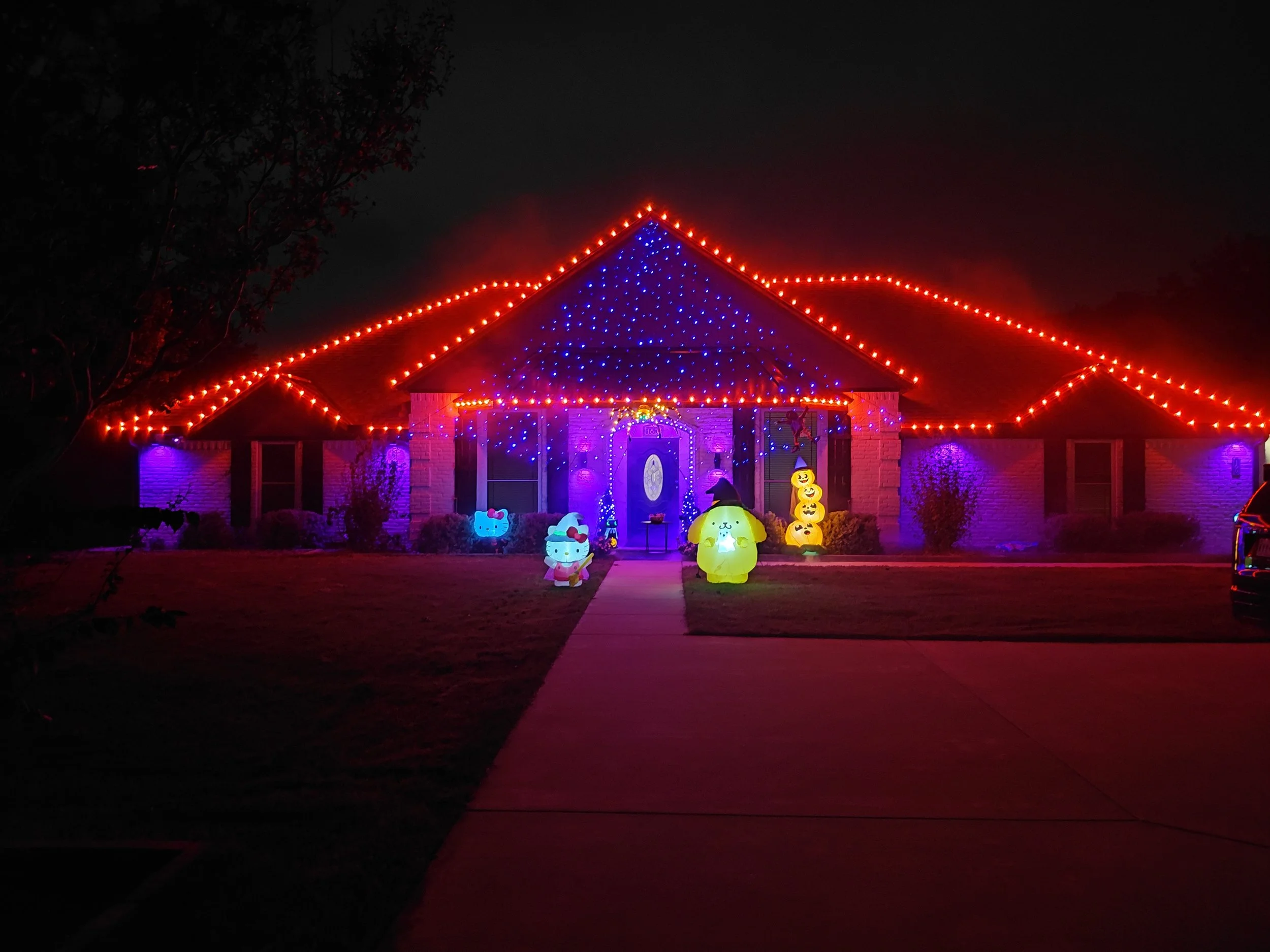 Halloween-themed holiday light installation with red and purple roofline lighting and inflatable decorations, Double Oak TX