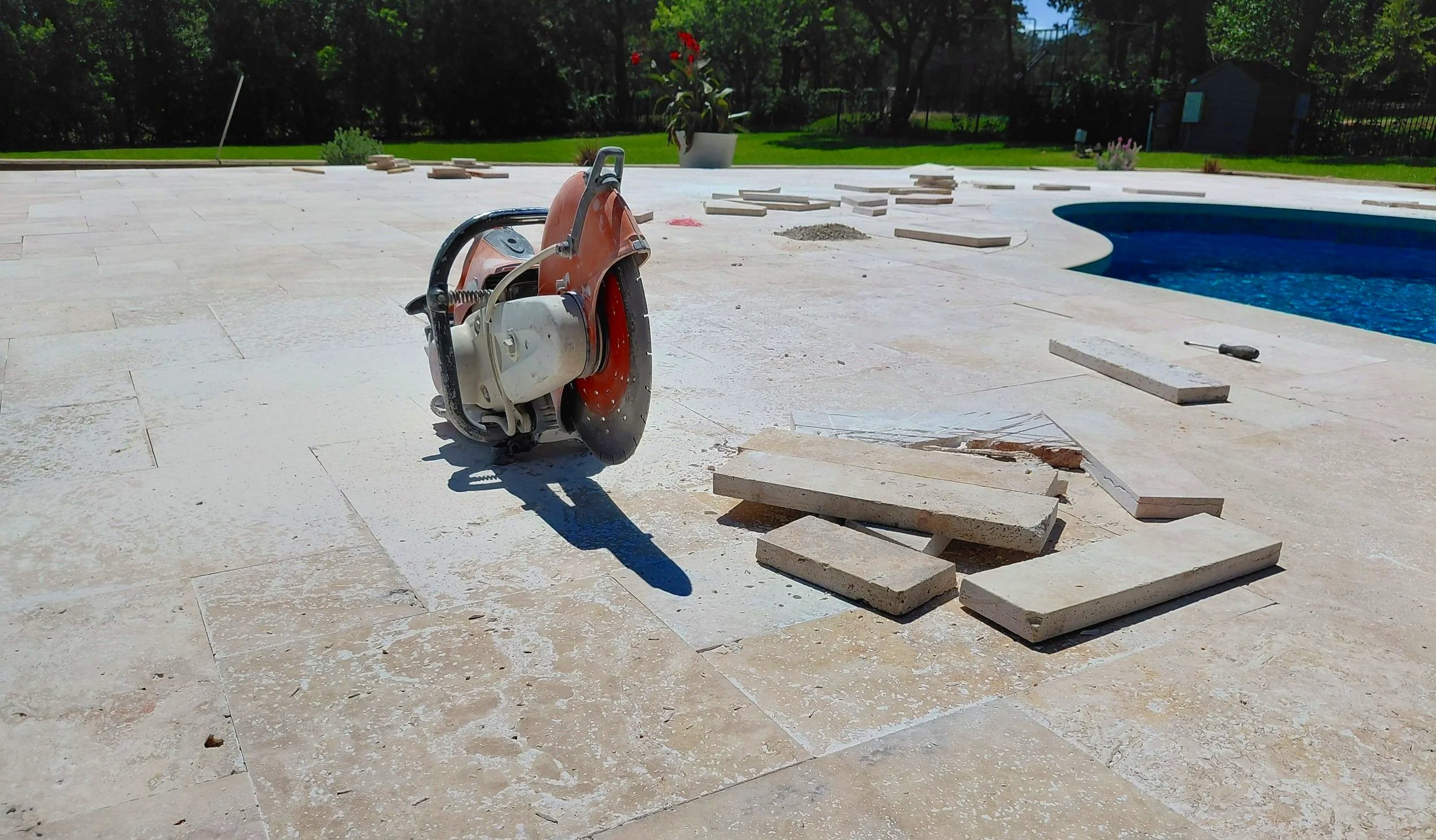Construction area featuring a power saw, scattered tiles, and a swimming pool in the background.