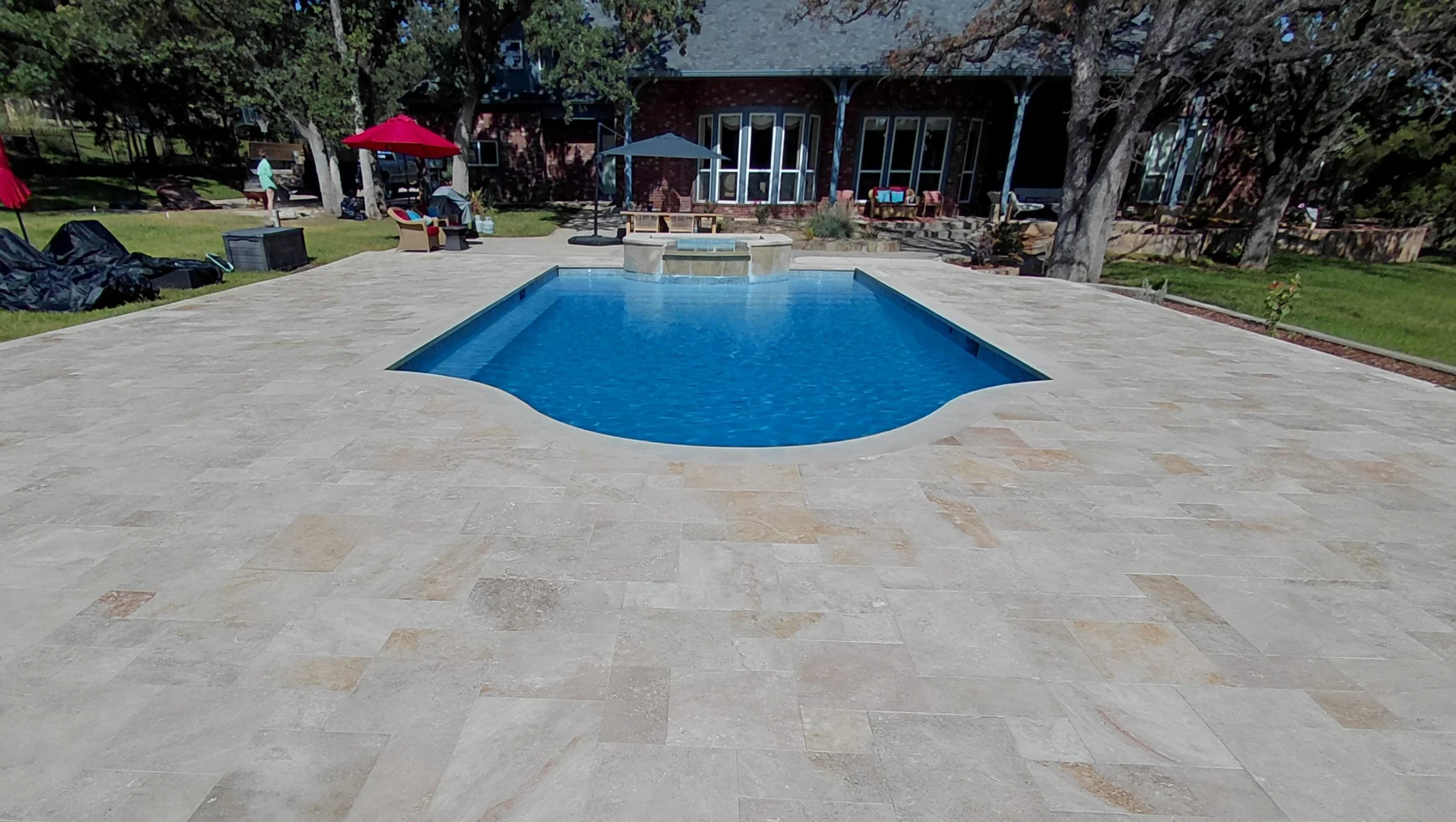 Backyard with a swimming pool, outdoor furniture, umbrellas, and a house with large windows in the background.