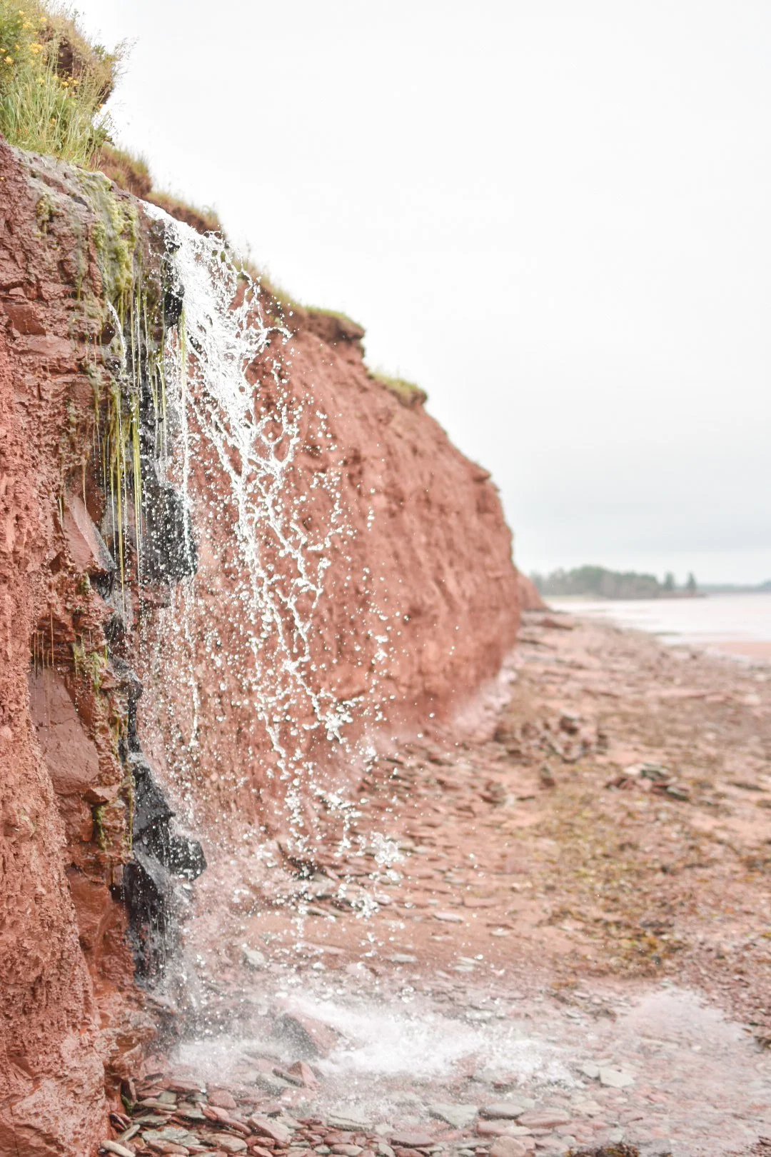 Water flowing over red clay cliffs on a cloudy day at a beach