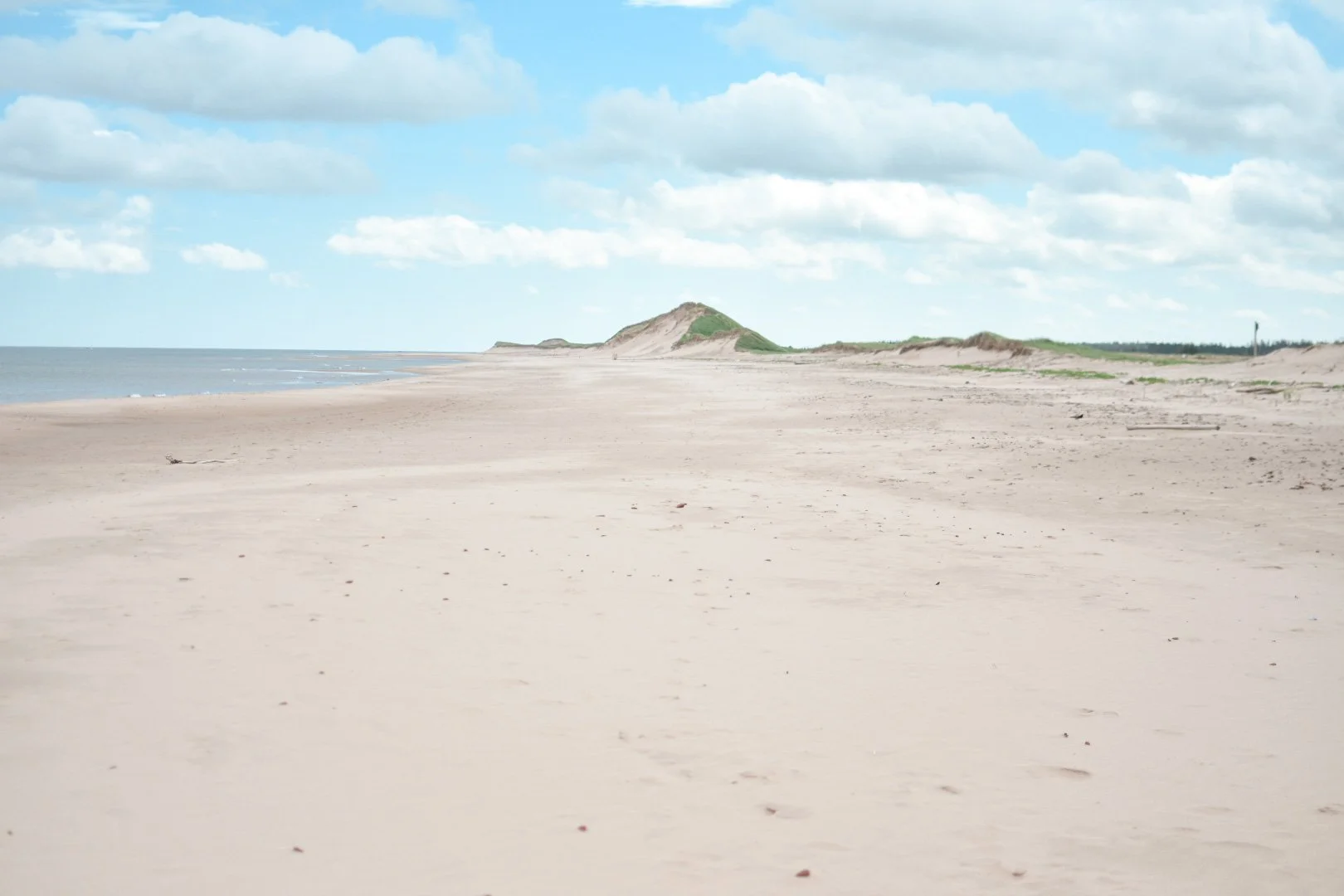 A deserted beach with sandy shoreline, with erosion cliffs in the background under a partly cloudy sky.