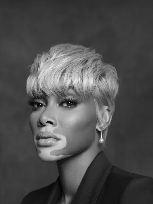 Black and white portrait of a woman with short, styled hair, wearing an earring and dark clothing.