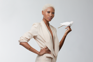 Woman with short platinum blonde hair wearing a beige blazer holding a white dove on her hand.