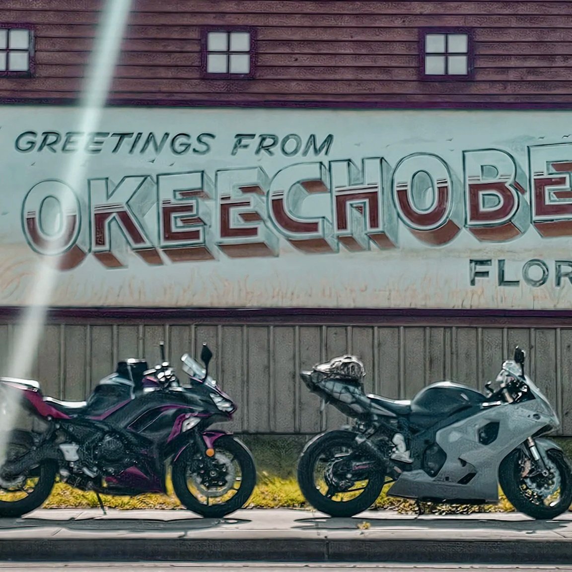 Two motorcycles parked in front of a mural that reads 'Greetings from Okeechobee, Florida.'