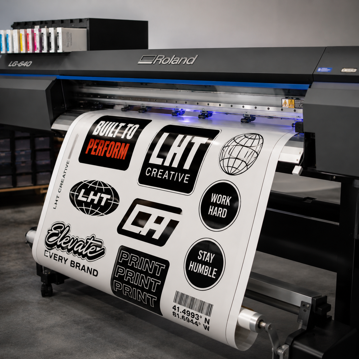 Large format printer producing a sheet with motivational and branding graphics including phrases like 'Built to Perform', 'LHT Creative', 'Work Hard', and 'Stay Humble', along with globe and barcode images.