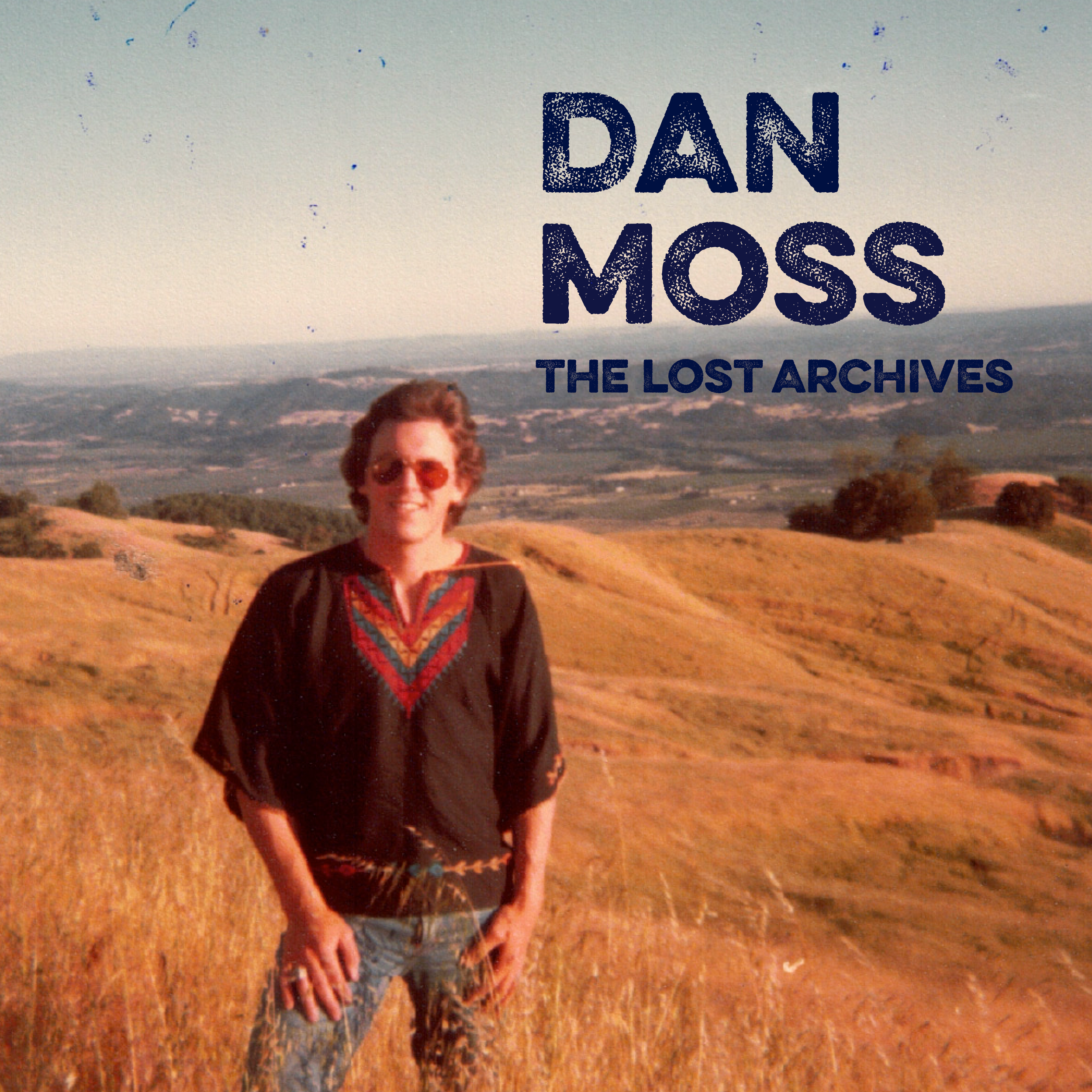 The Lost Archives album cover, a person with sunglasses smiling, standing outdoors in a mountainous landscape with dry terrain.