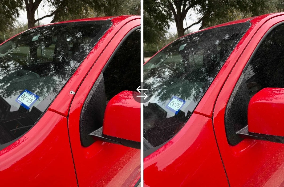 Close-up of a red pickup truck's windshield, side mirror, and front fender with tree reflections on the windshield.