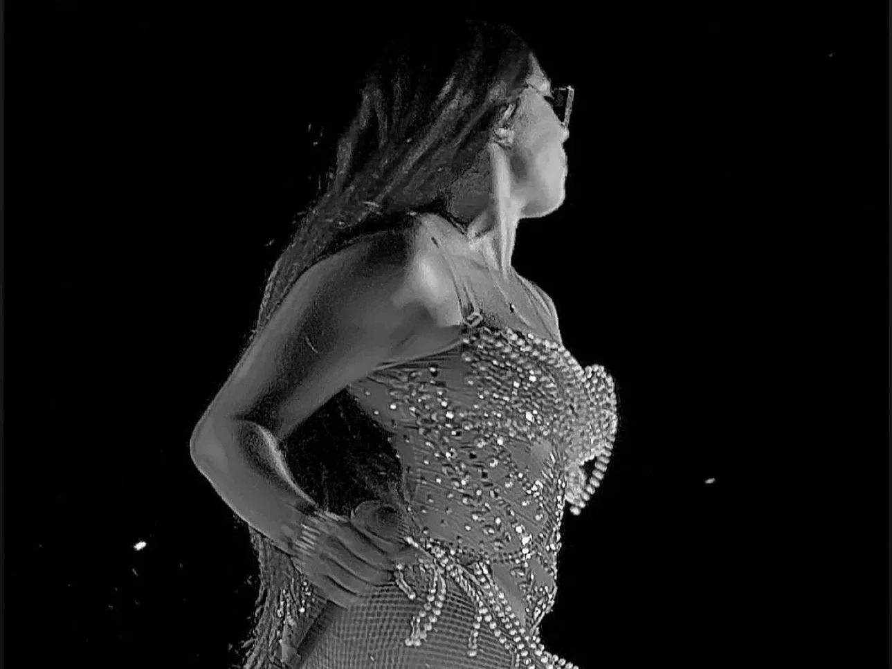 Black and white photo of Jadel in a sparkling dress, wearing sunglasses, standing against a dark background. Belize International Music & Food Festival 2023