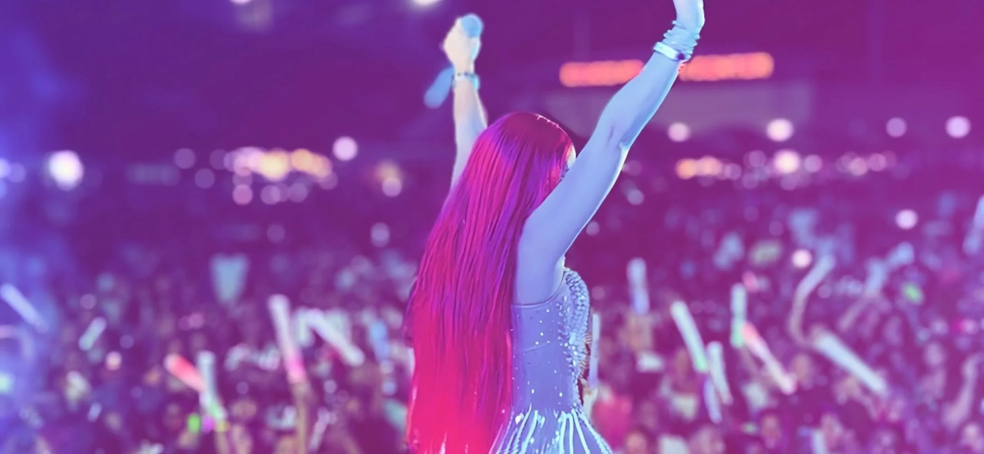 Jadel with long pink hair on stage with arms raised, colorful lights and a blurred crowd in the background. Belize International Food & Music Festival