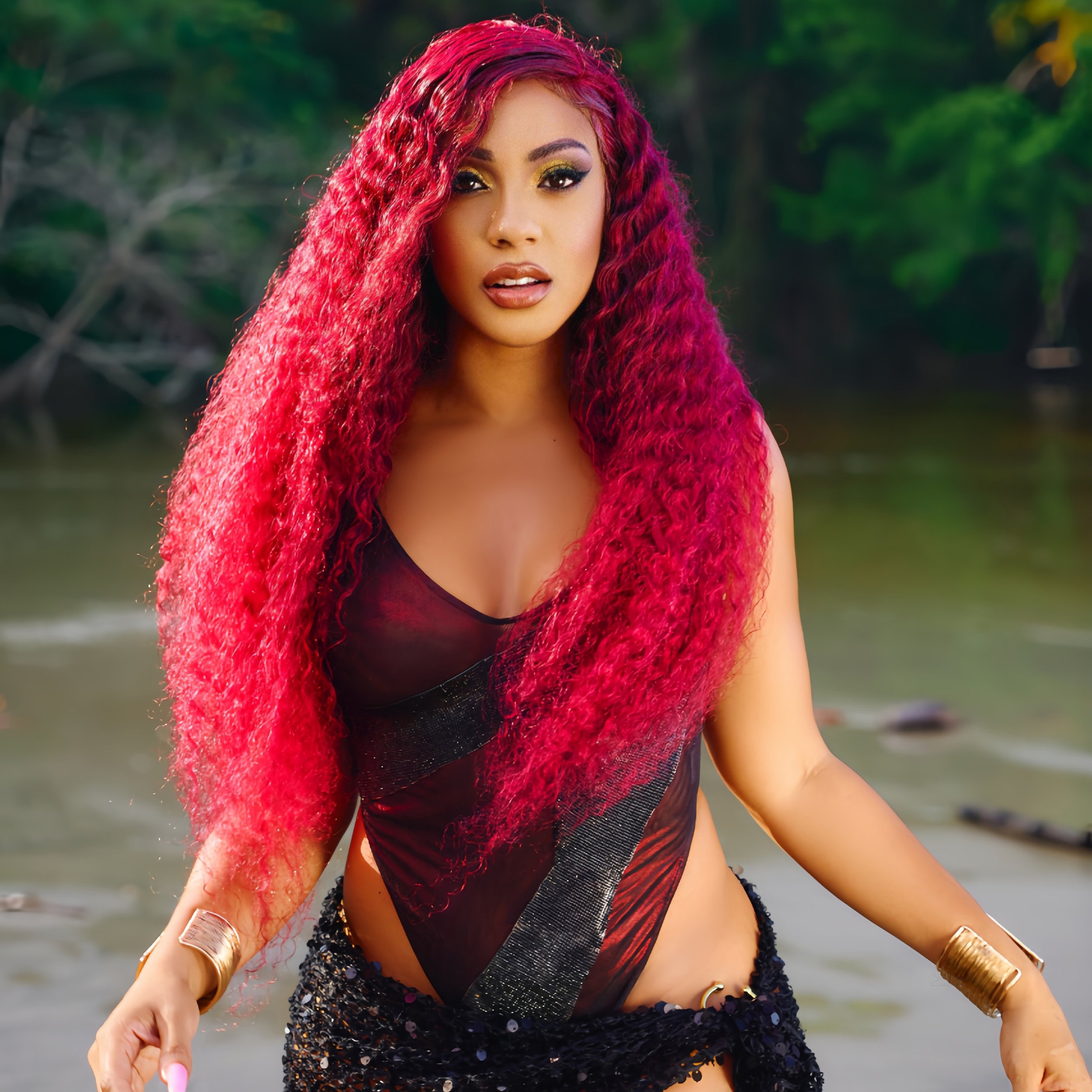 Jadel - Don't Be Mistaken Album Front Cover. A woman with curly, bright pink hair wearing a black and red dress, standing near a body of water with a blurred green forest in the background.
