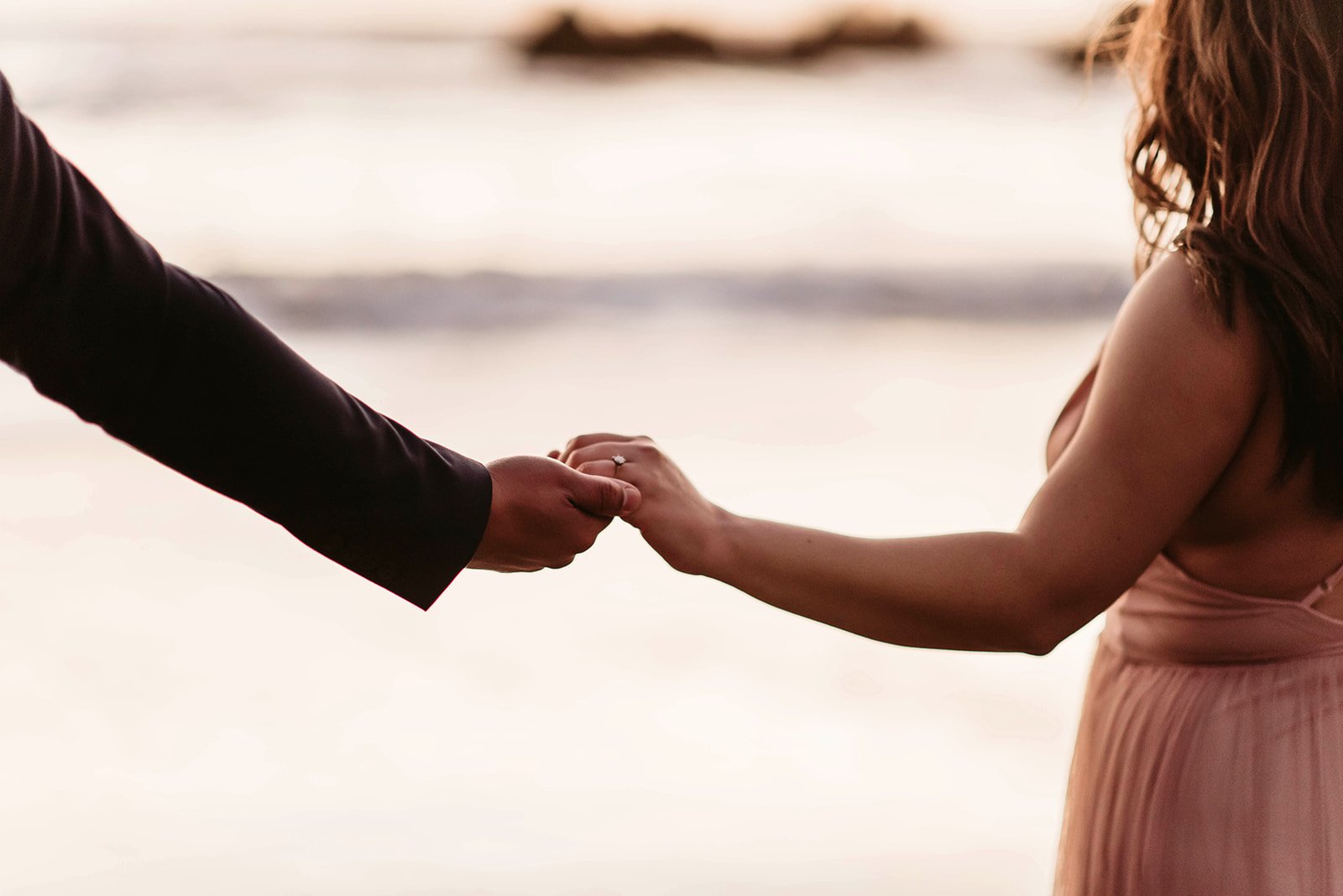 A man and woman holding hands on a beach at sunset.