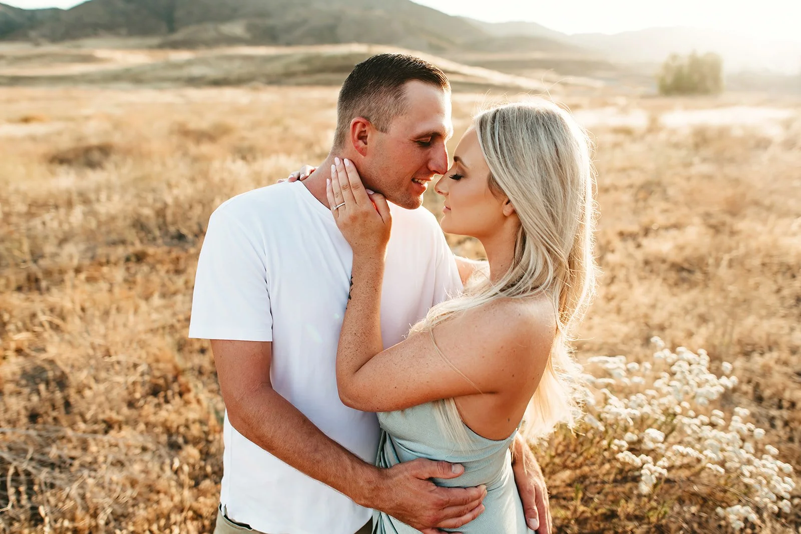 A couple embracing in a field at sunset, touching foreheads.
