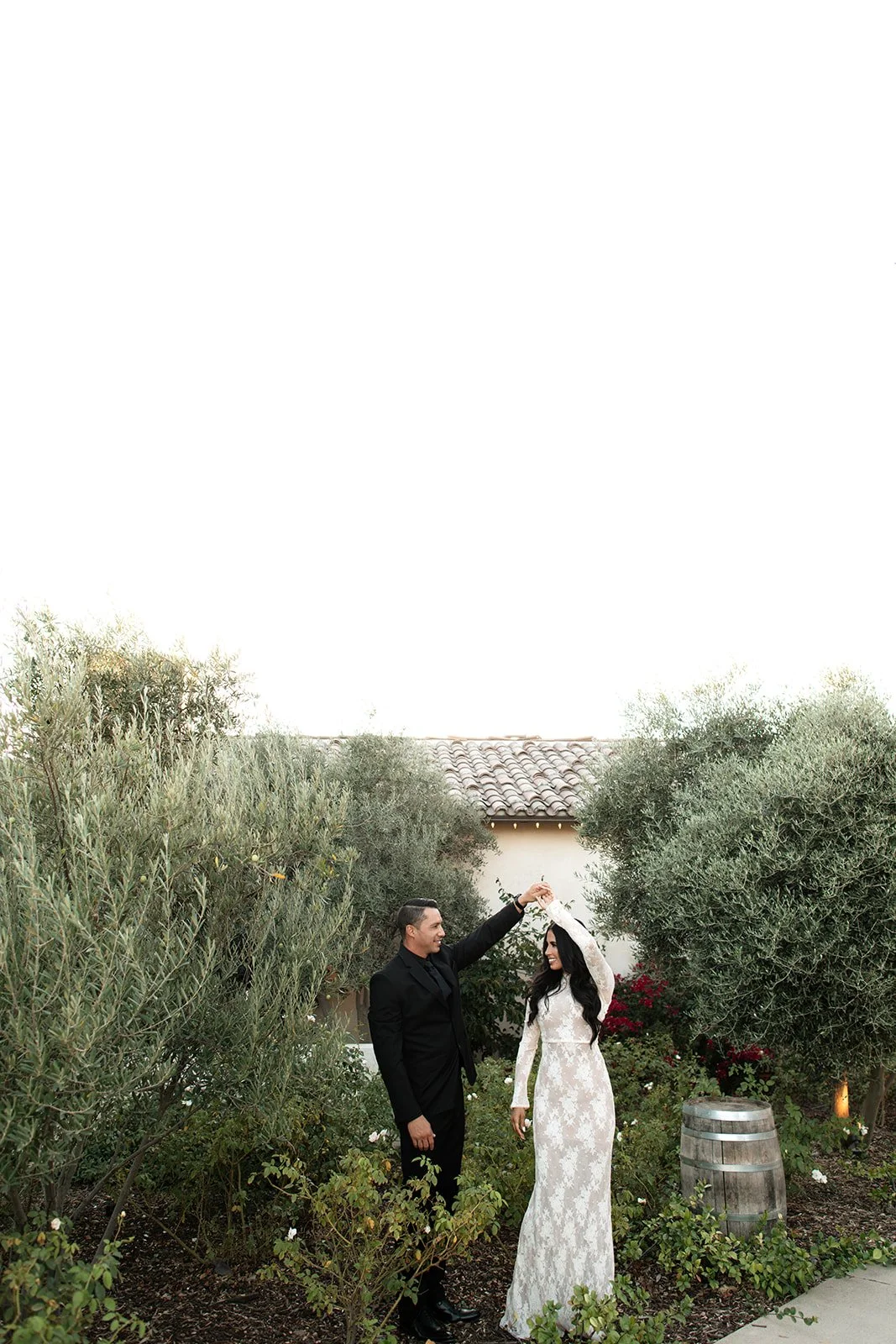 A bride and groom dancing outdoors surrounded by greenery, with the groom holding the bride's hand in a dance pose.
