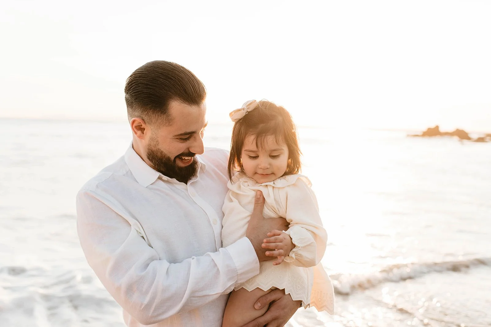 Man holding a young girl at the beach during sunset
