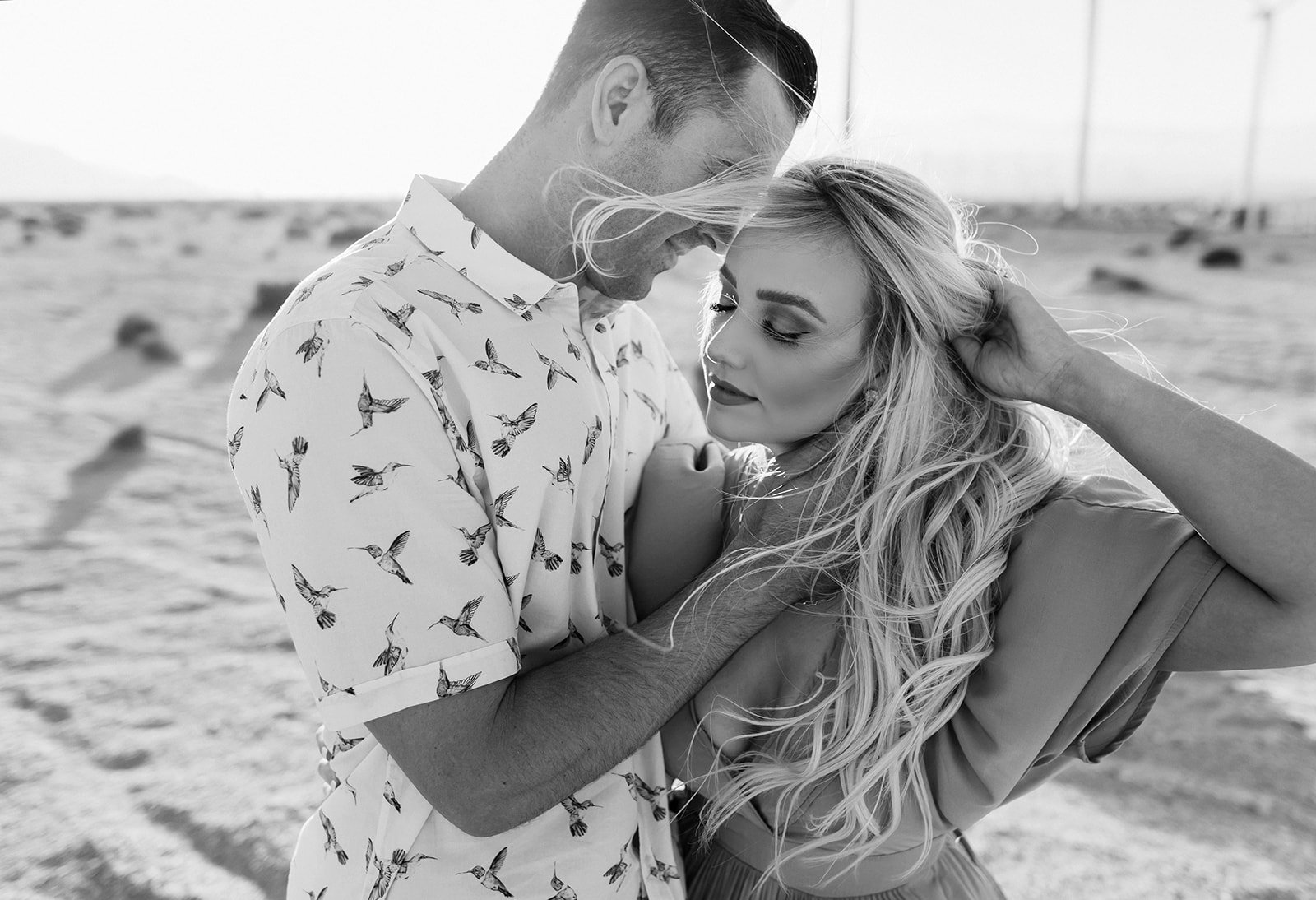 A couple in an embrace on the beach, with the man gently holding the woman's face and she leaning into him, both with closed eyes.