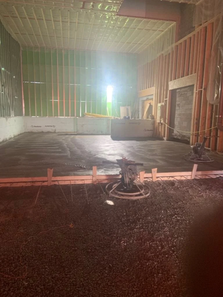 Construction site with freshly poured concrete floor, framing on the walls, and construction tools.
