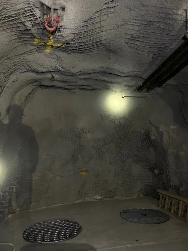 Underground construction site with rocky walls, plumbing pipes, and grates on the floor.