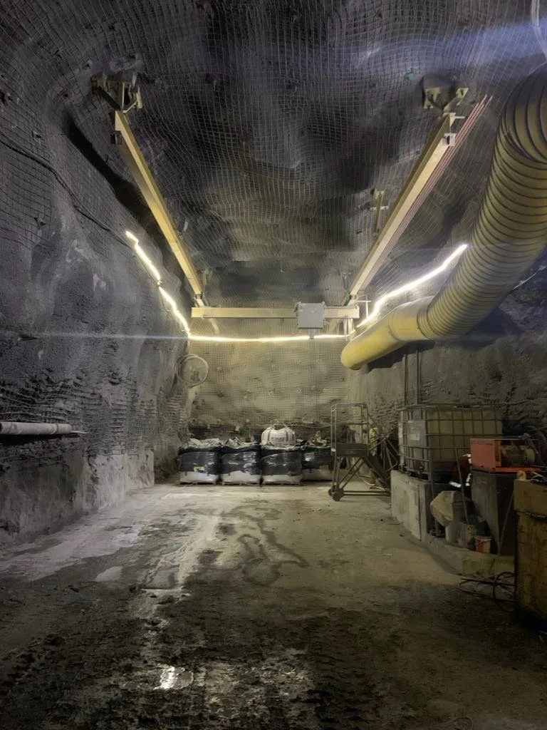 Underground construction site with black walls, large yellow ventilation pipe, and construction equipment.