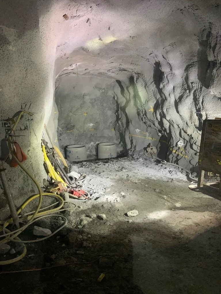 Underground tunnel or cave under construction with construction tools, yellow hoses, and two white containers inside.