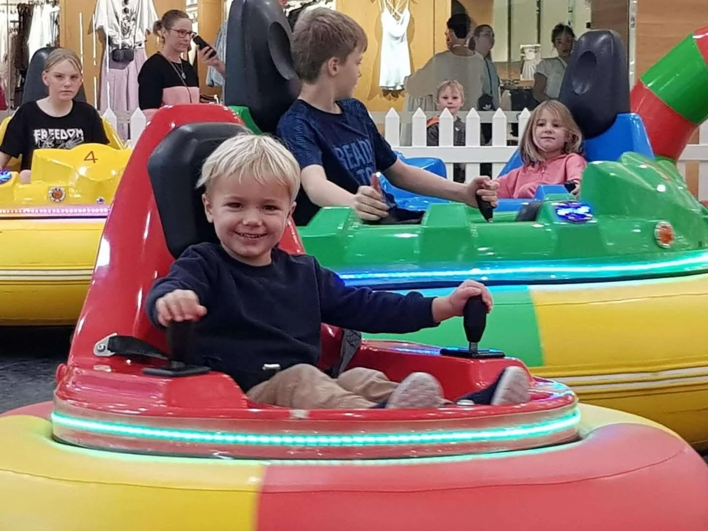 Children riding colorful bumper boats at an indoor amusement park.