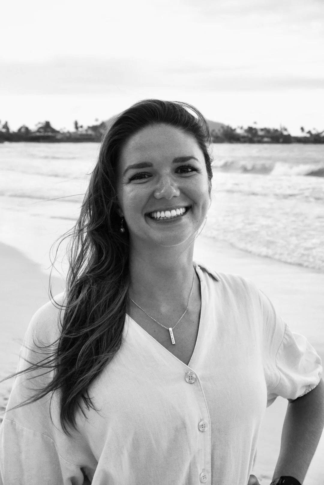Vineta Gleba, counselor and coach. A  kind, smiling woman with long wavy hair standing on a beach with ocean waves in the background.