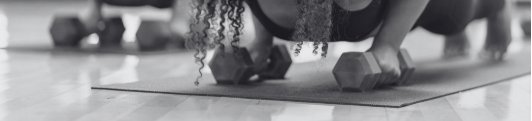 Close-up of a woman doing push-ups with dumbbells on a yoga mat in a gym.